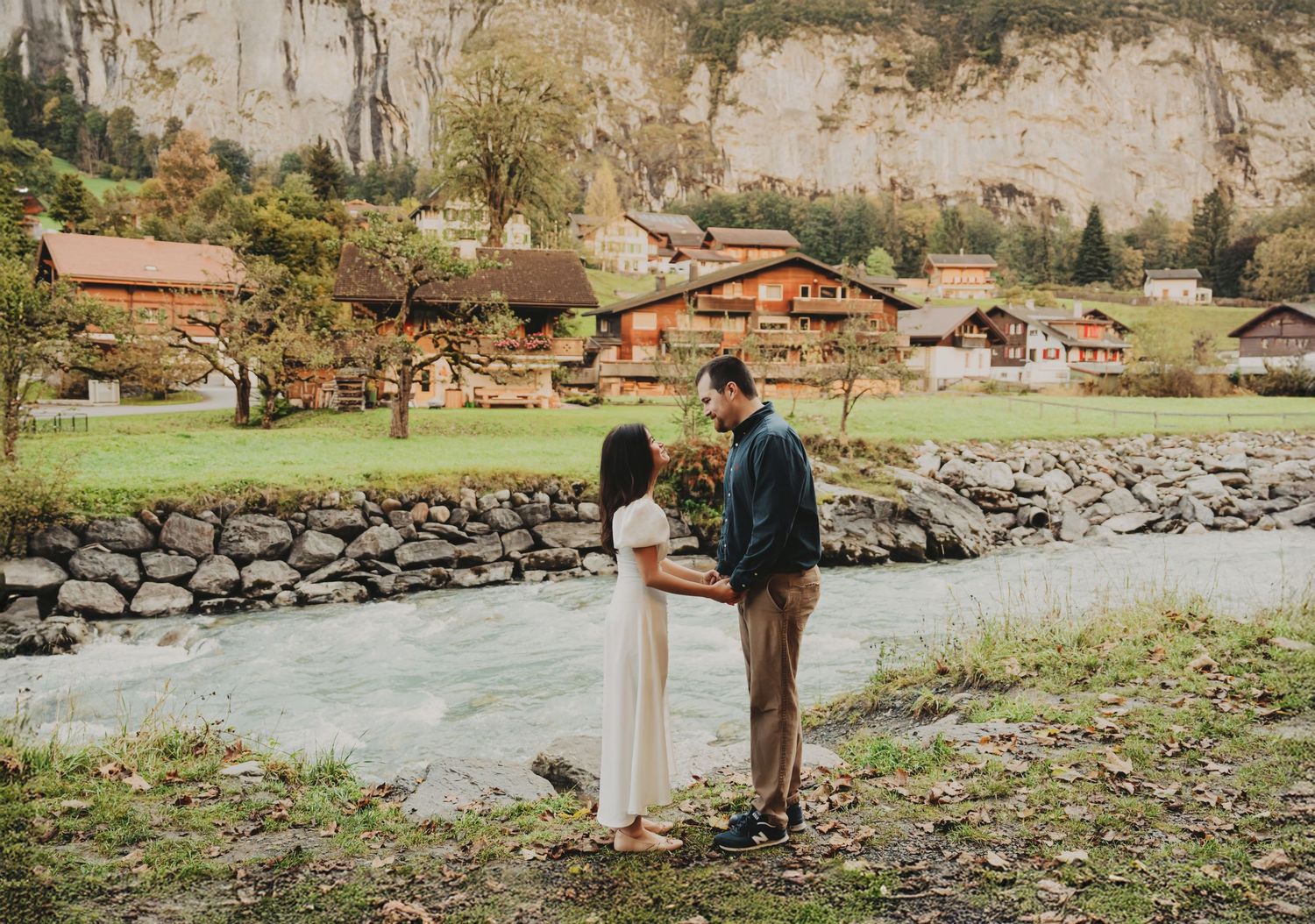 Couple standing by a rushing alpine river surrounded by Swiss chalets and mountains.
