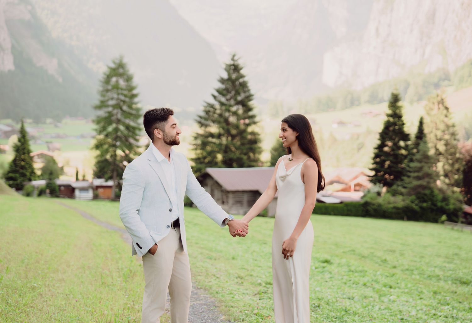 Couple holding hands and gazing at each other on a scenic Alpine meadow pathway.
