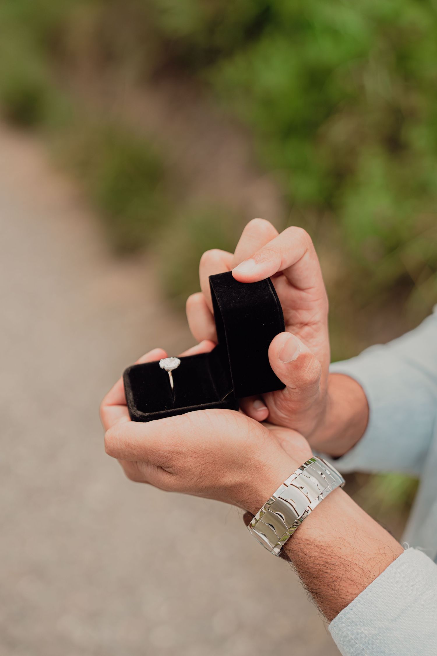 Close-up of hands holding open a black ring box with a diamond engagement ring inside.