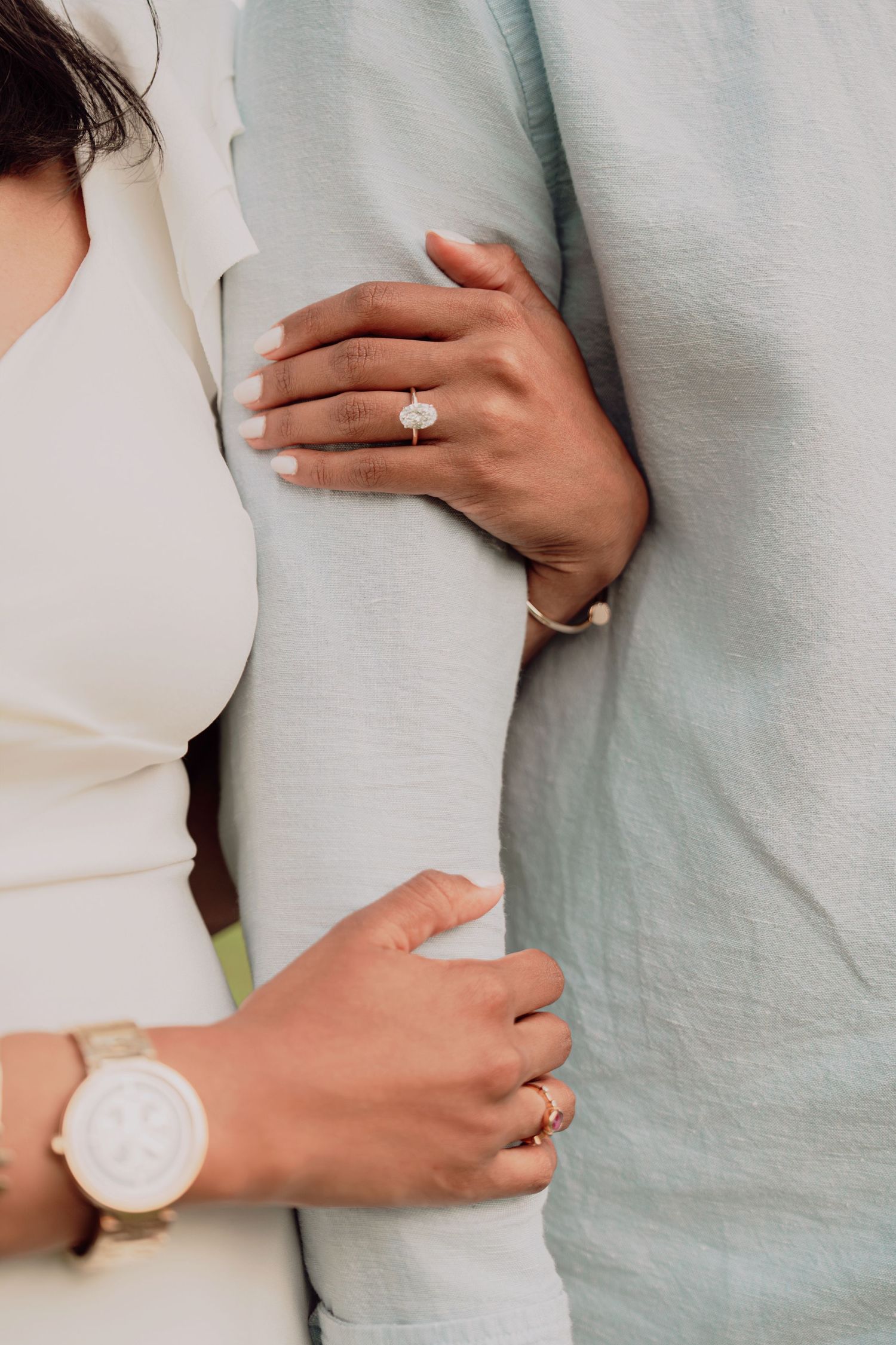 Close-up of a bride's hands with diamond engagement ring and gold watch holding her partner's arm.