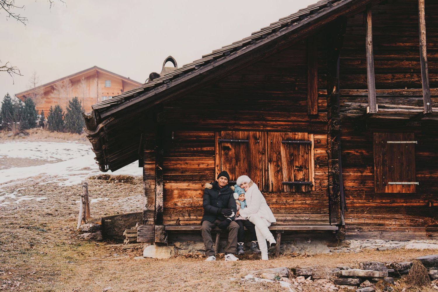 Family sitting together on the porch of a charming rustic wooden chalet in winter.