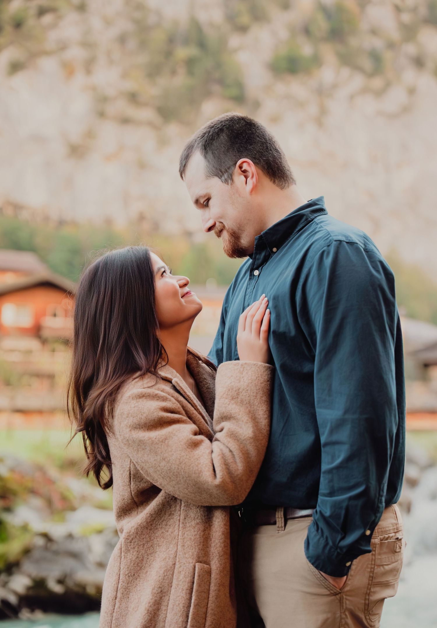 Smiling couple gazing into each other's eyes near a rocky alpine river in autumn.