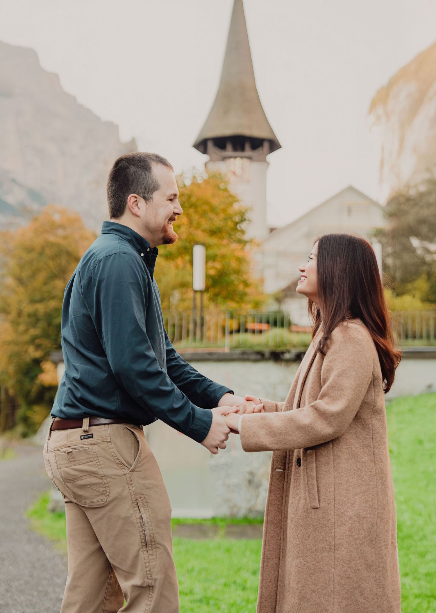 Happy couple holding hands and laughing near a historic Swiss church tower in autumn.