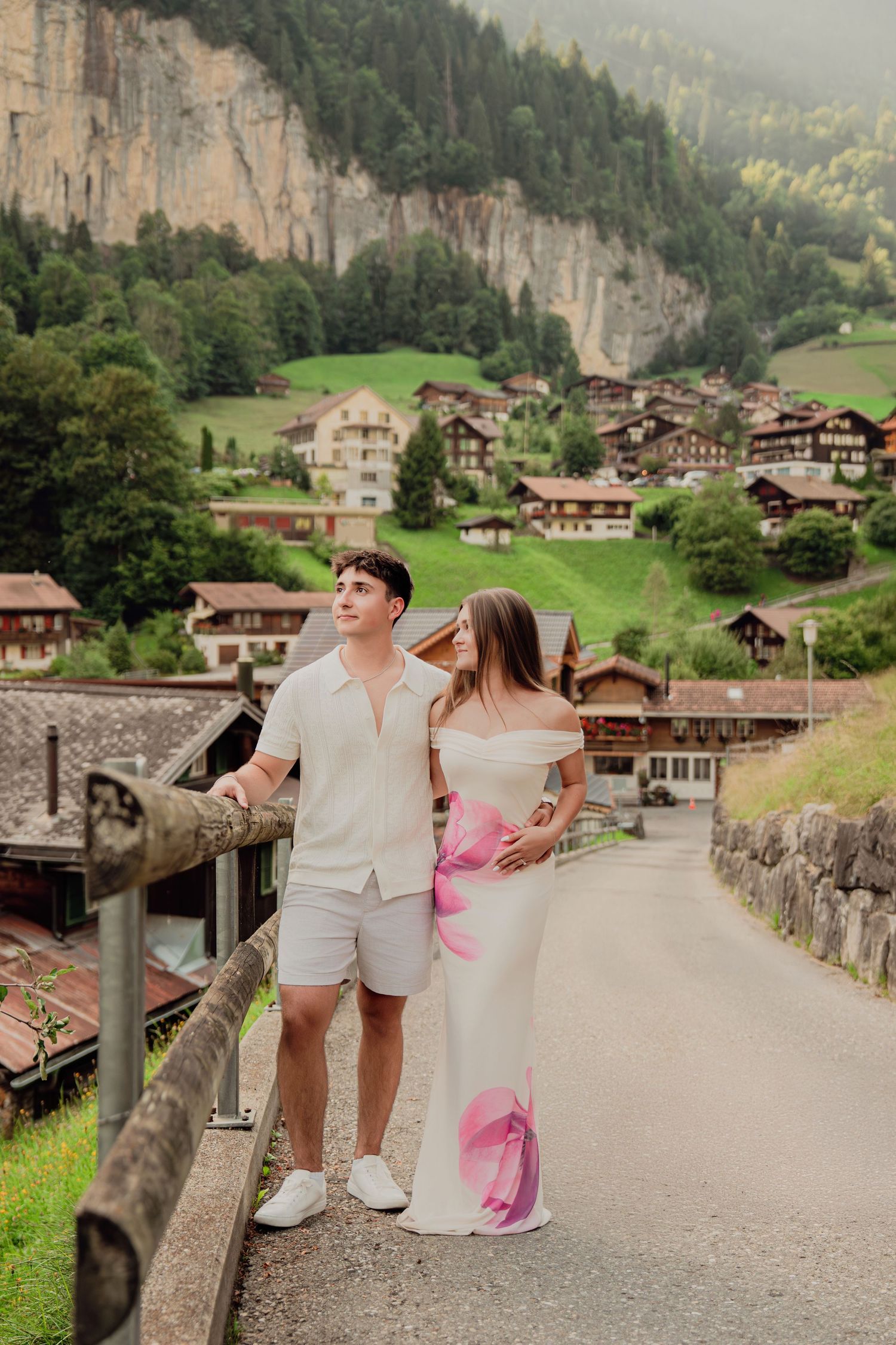 Couple posing on a bridge in Lauterbrunnen Switzerland with alpine village and green mountains behind.