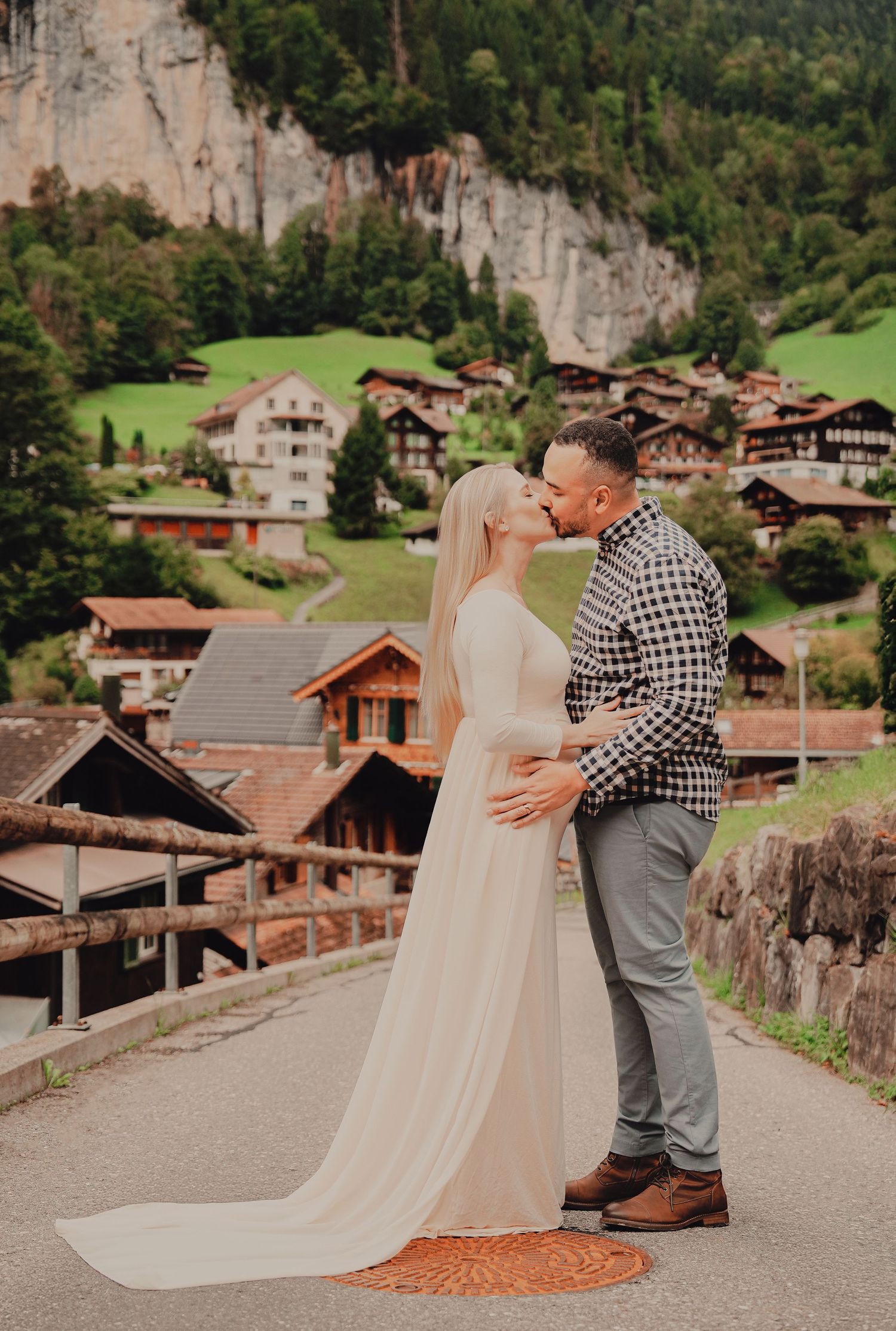 Couple sharing a kiss on a bridge in Lauterbrunnen Switzerland with alpine village and waterfall backdrop.