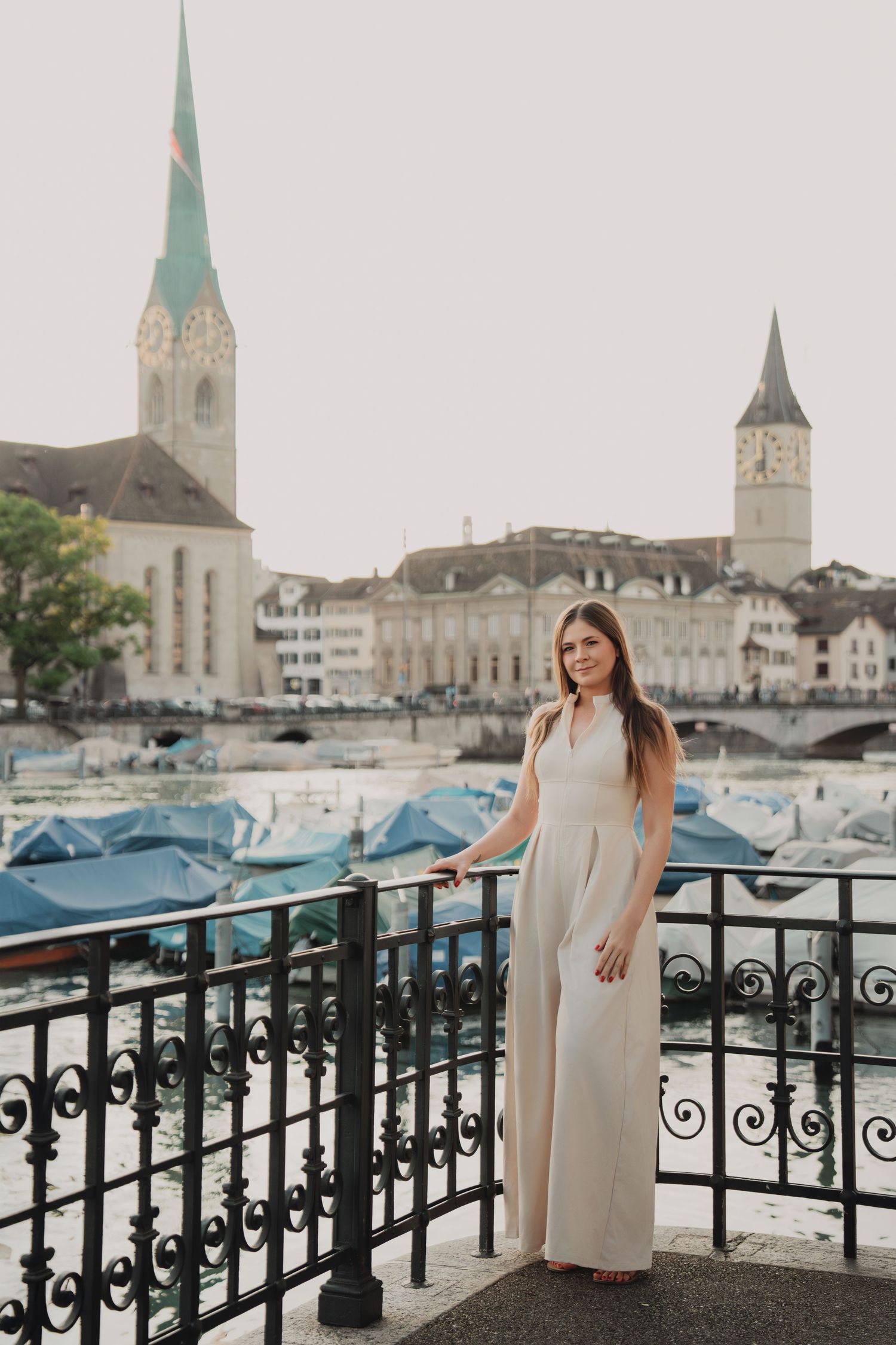Young woman in white dress posing on balcony with Zurich skyline and church towers.
