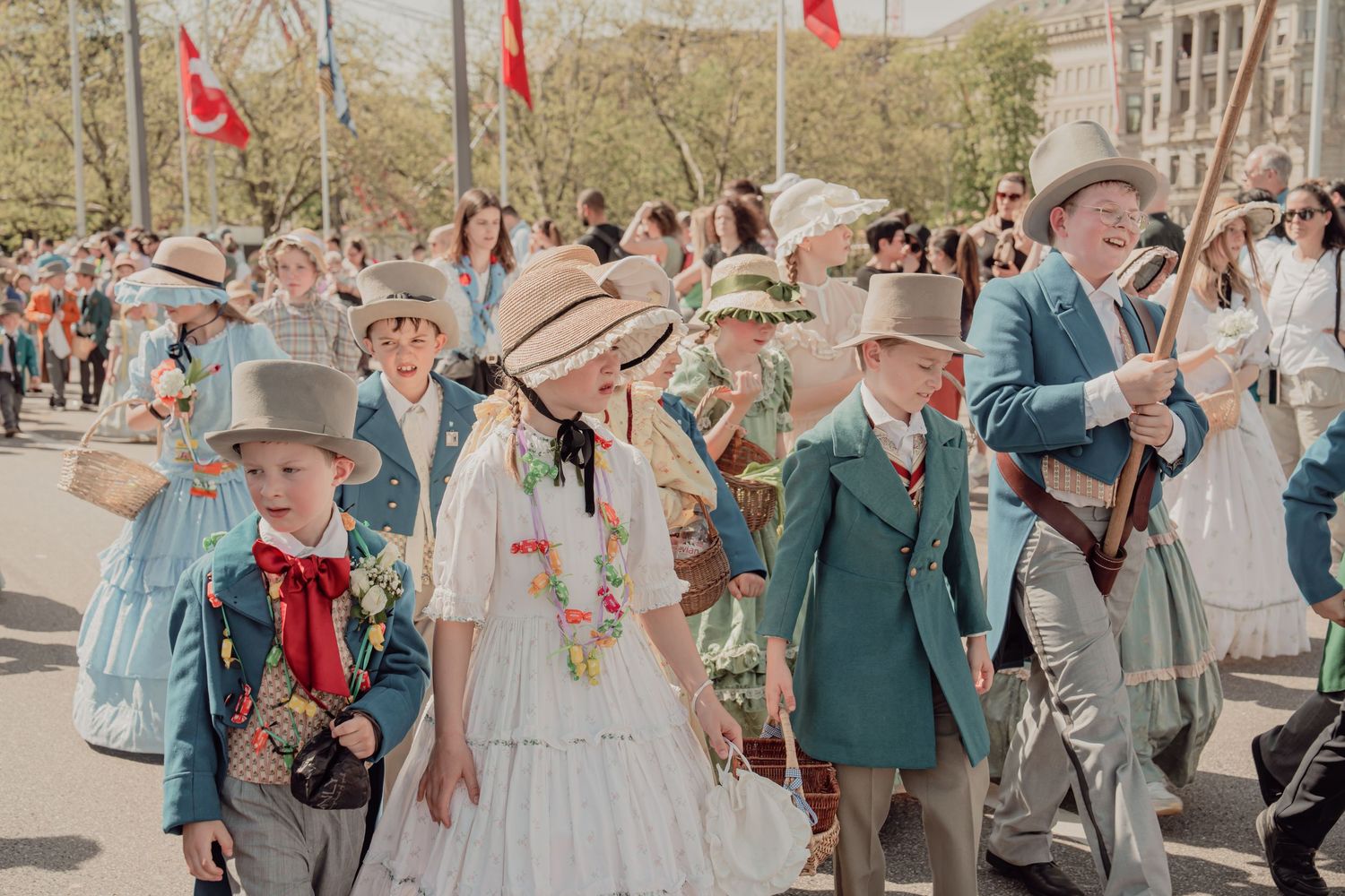 Children and adults in Victorian period costumes with straw hats march in traditional spring parade.