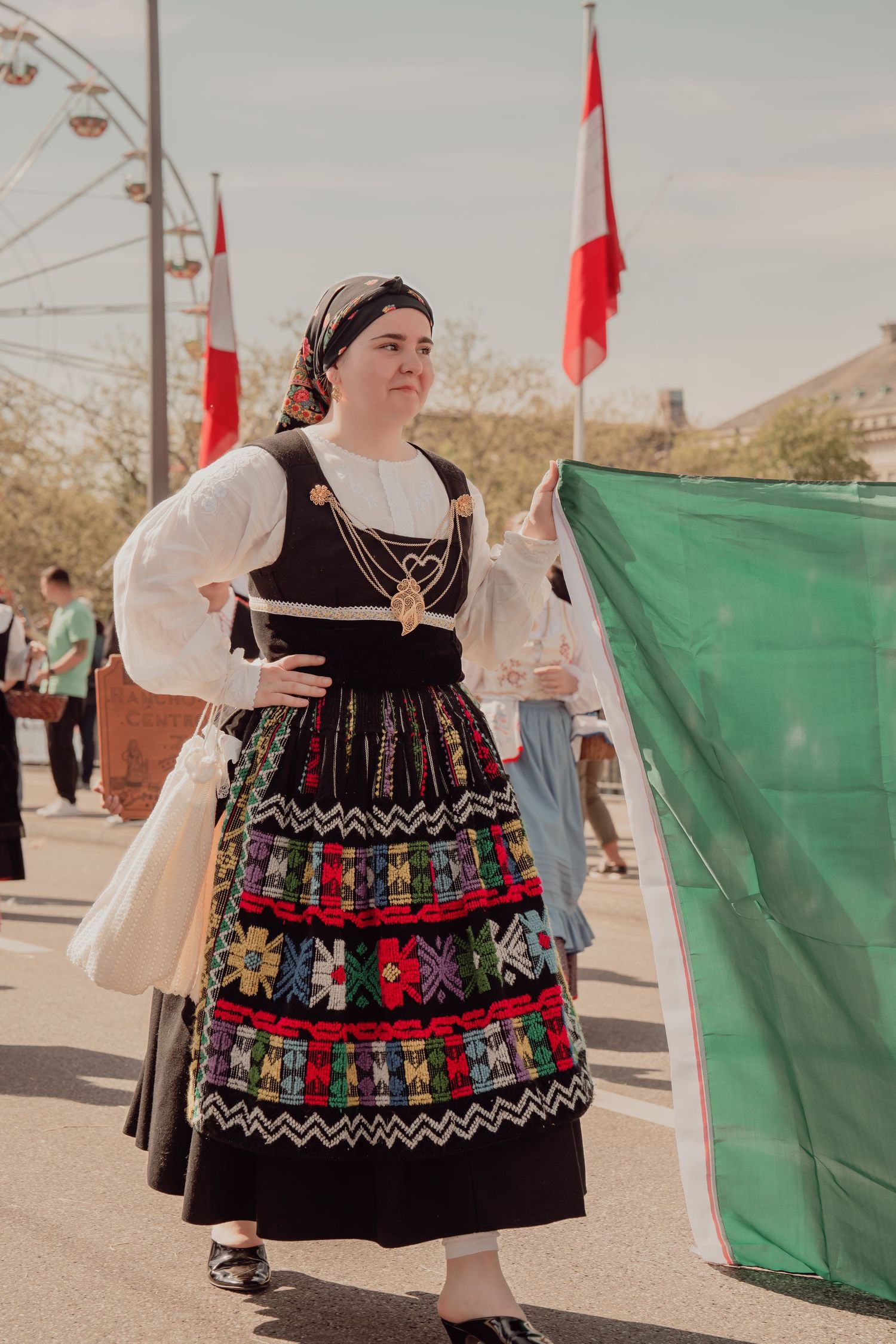 Woman in traditional Swiss regional folk costume holding green flag at outdoor festival.