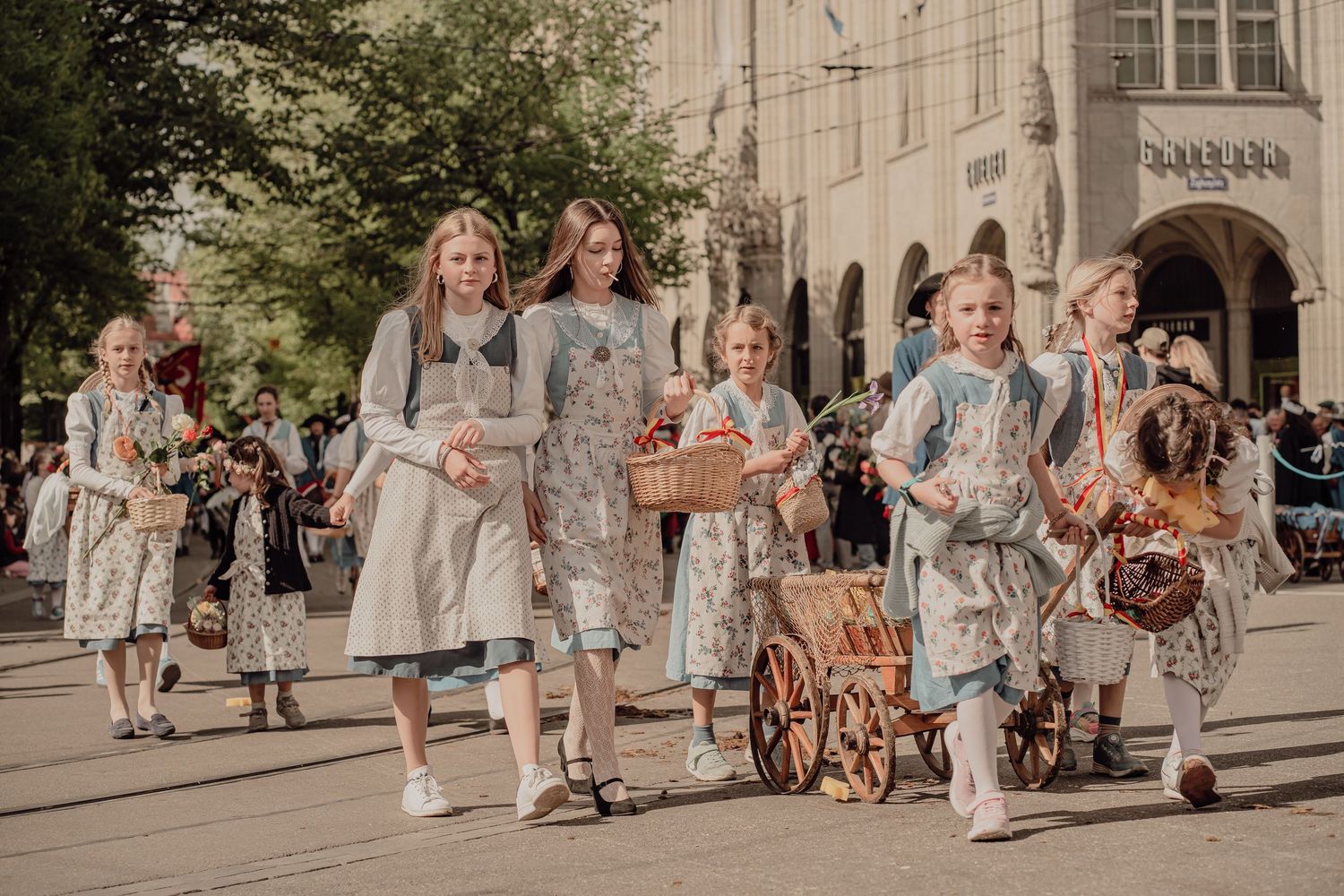 Women and children dressed in matching floral folk dresses walk in a traditional cultural parade.