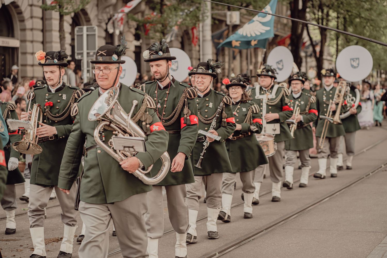 Musicians in green Alpine folk costumes playing brass instruments while marching in a traditional Swiss street parade.