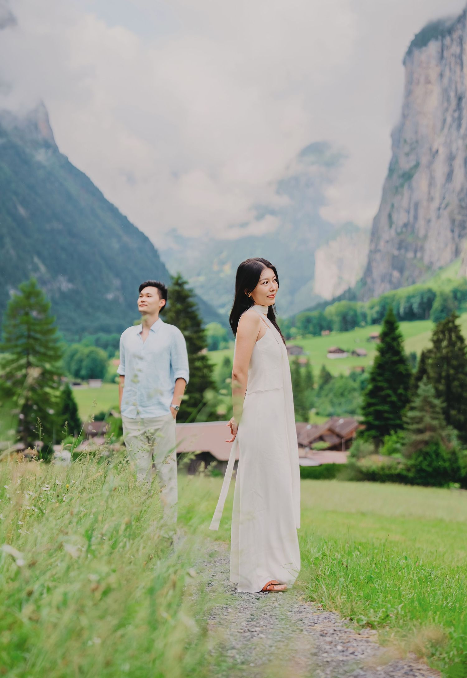 Woman in white dress looks back at camera while couple walks on a path in scenic Lauterbrunnen, Switzerland.