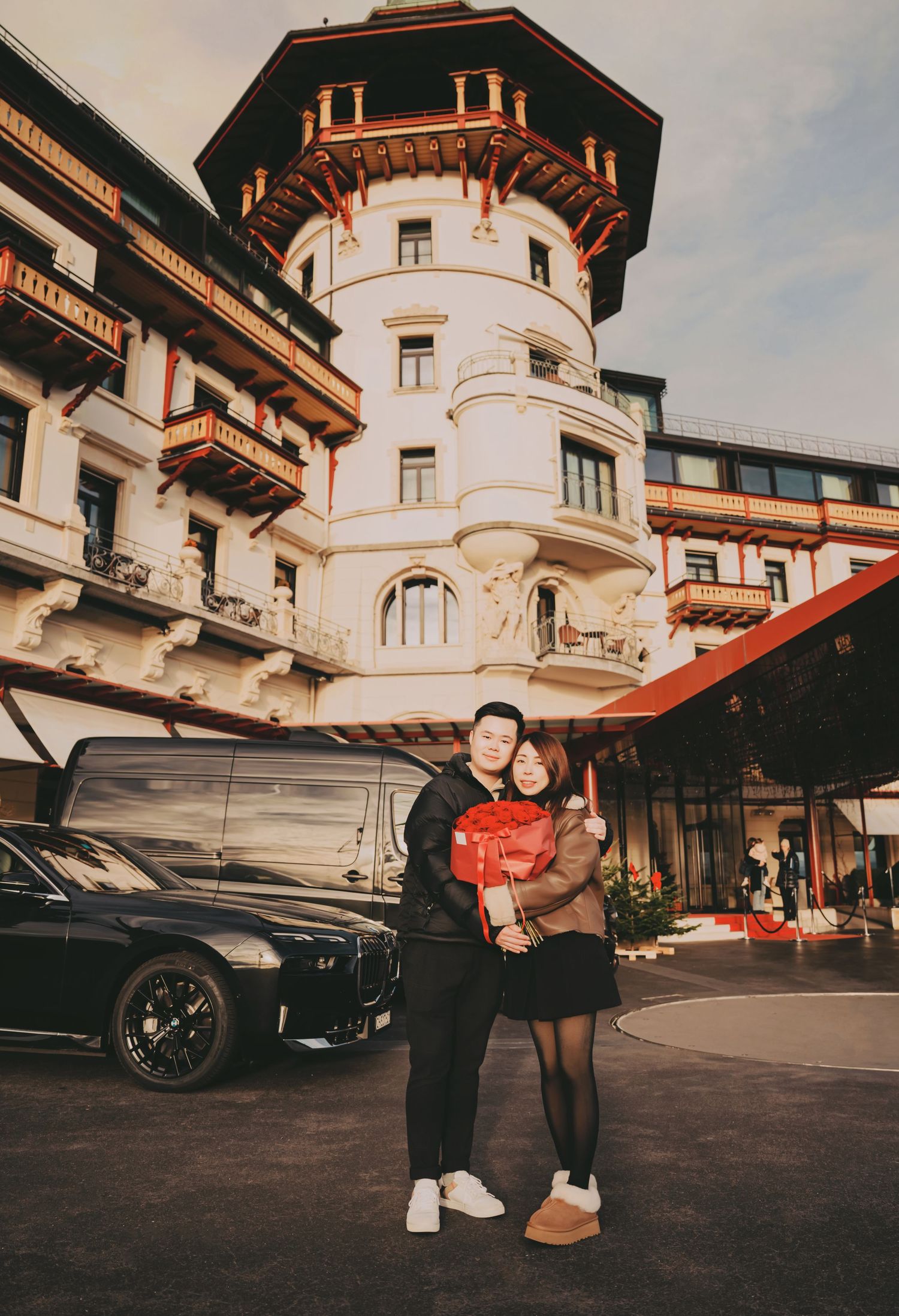 Couple posing in front of ornate white European castle hotel with black BMW.