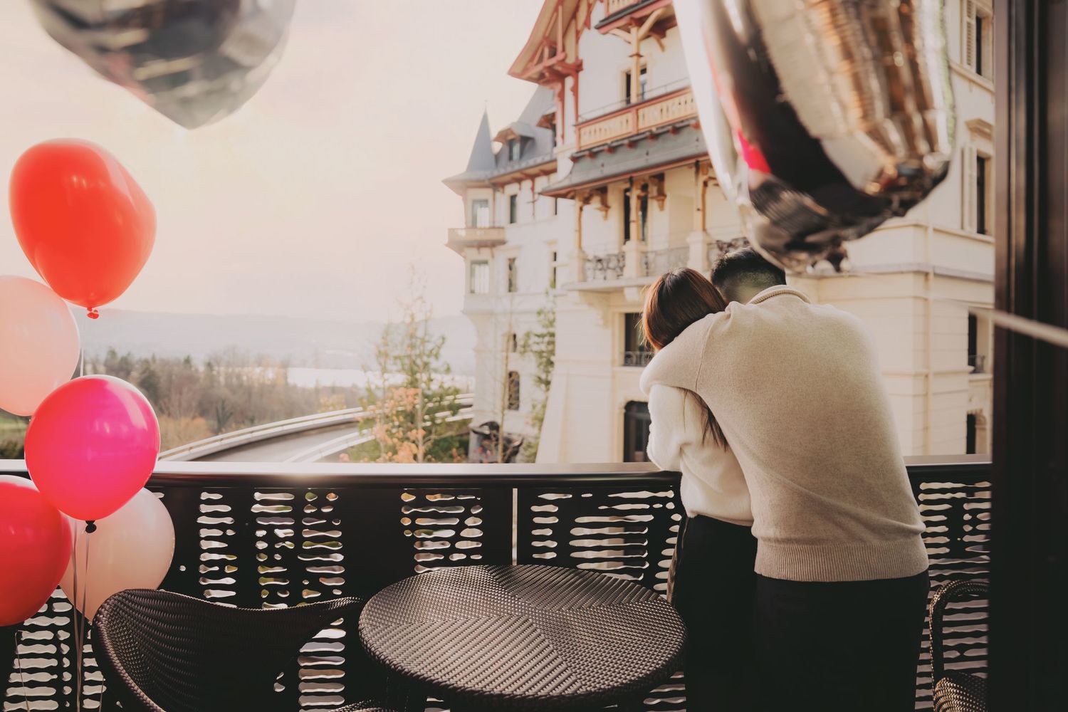 Person leaning over balcony railing with colorful balloons beside them at a luxury hotel.