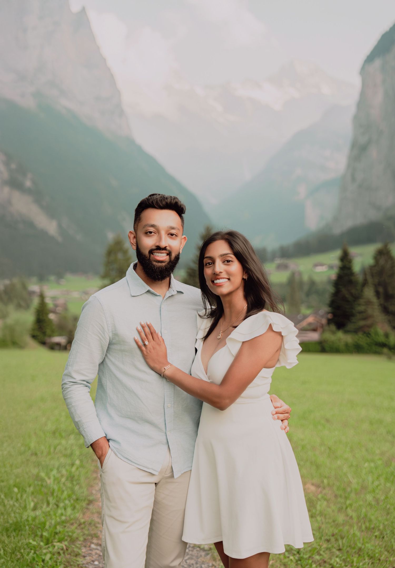 Smiling couple posing together in front of a stunning Swiss Alpine valley with dramatic mountain peaks.