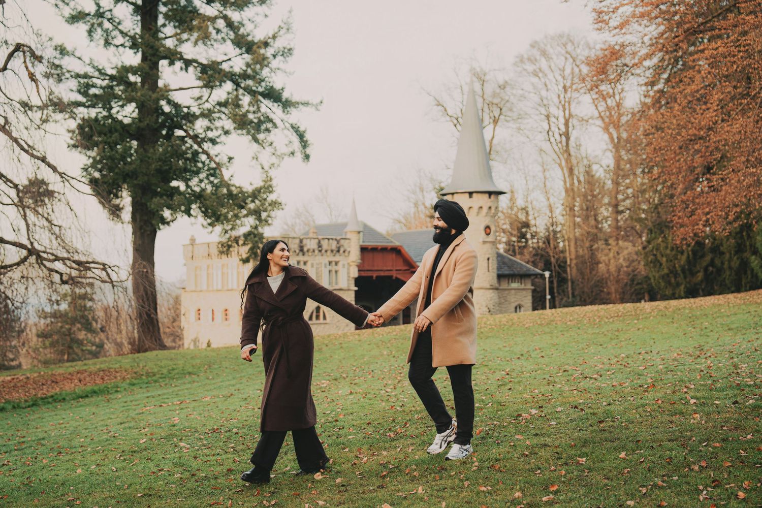Couple holding hands and dancing on a green lawn with a castle in the background during autumn.