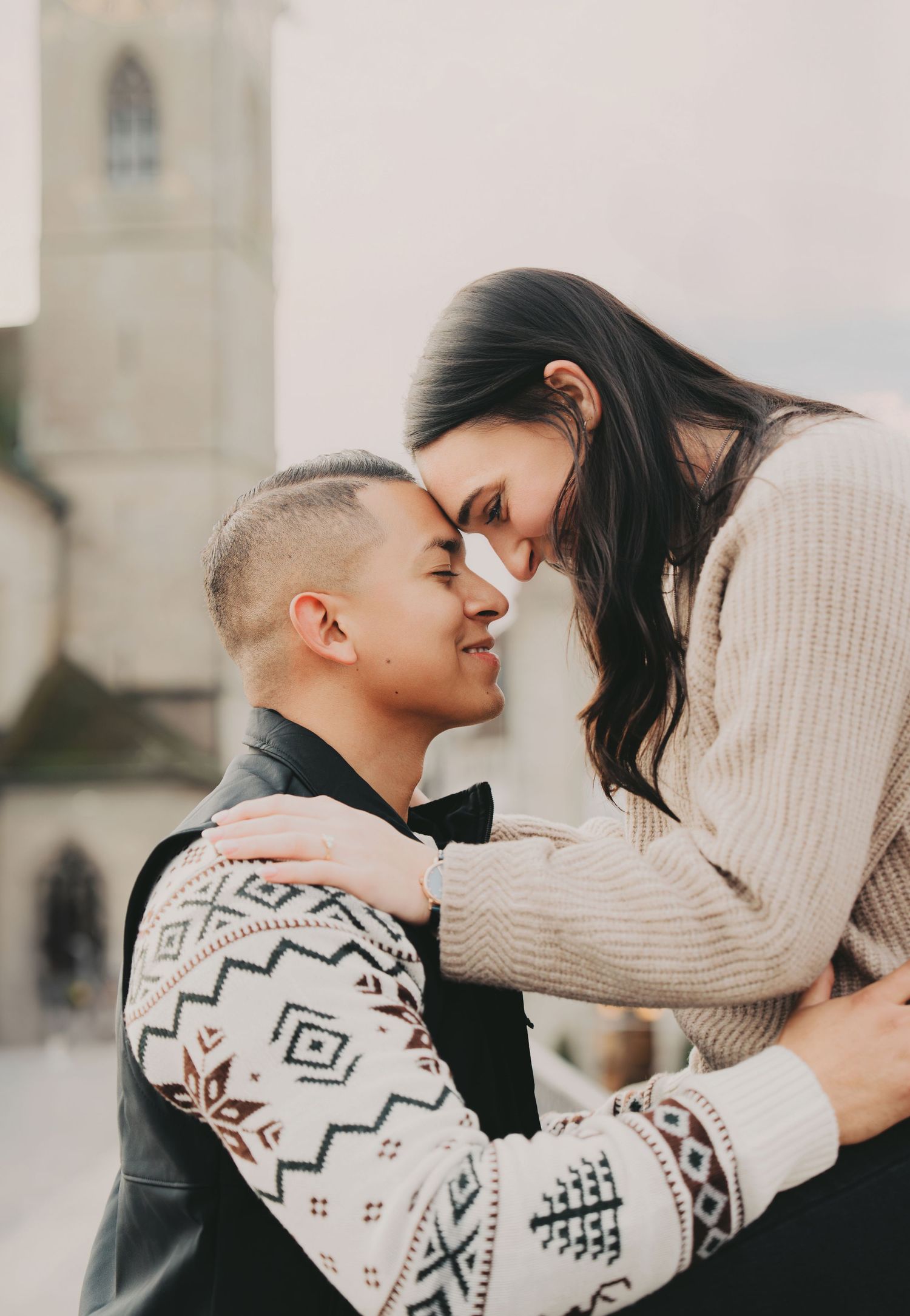 Couple touching foreheads in a tender romantic moment with a church steeple in the background.