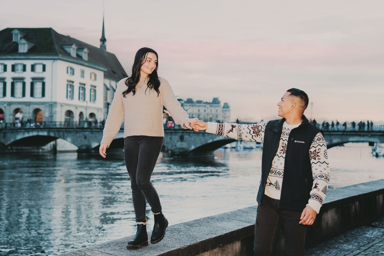 Woman balancing on a wall holding mans hand by the Limmat River in Zurich, Switzerland.