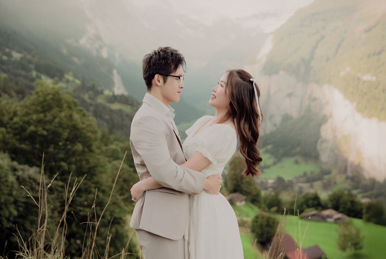Happy couple embracing and smiling with a breathtaking Swiss valley and waterfall landscape behind them.