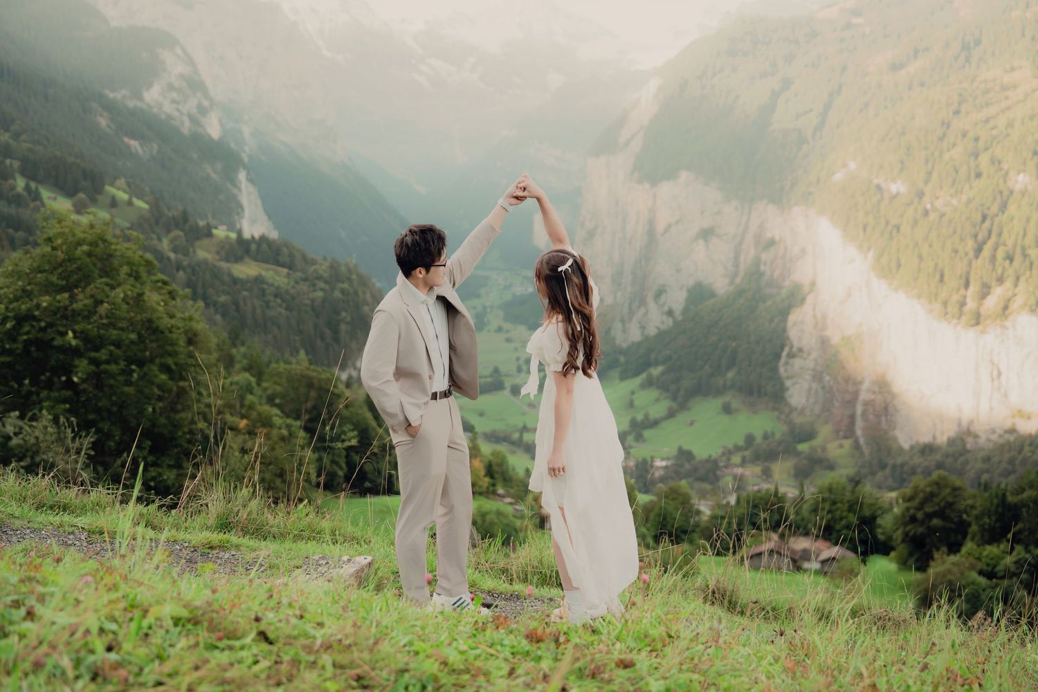 Couple dancing romantically with raised hands overlooking stunning Lauterbrunnen waterfall valley in Switzerland.