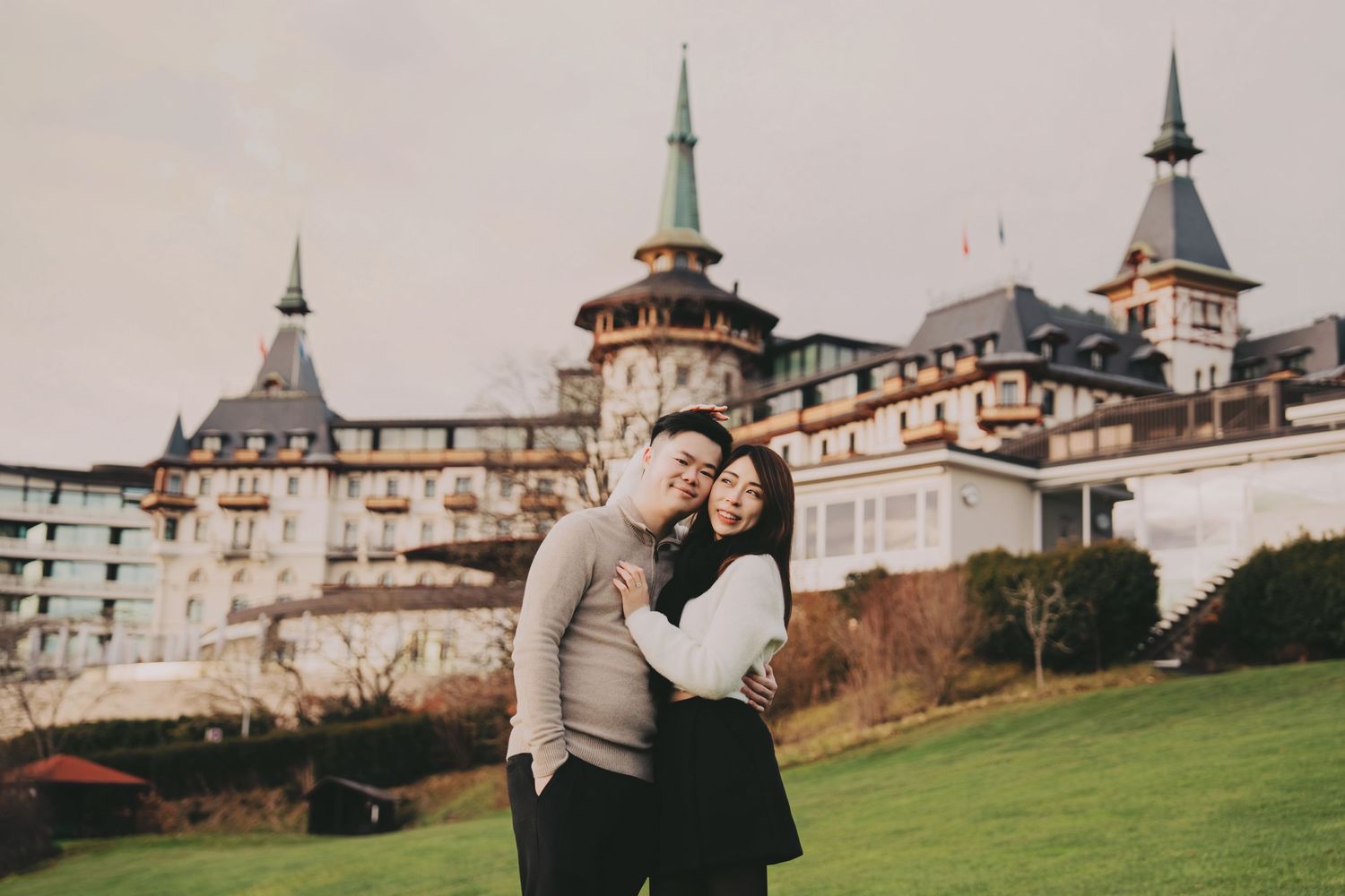 Happy couple embracing and smiling on green lawn before grand European castle building.
