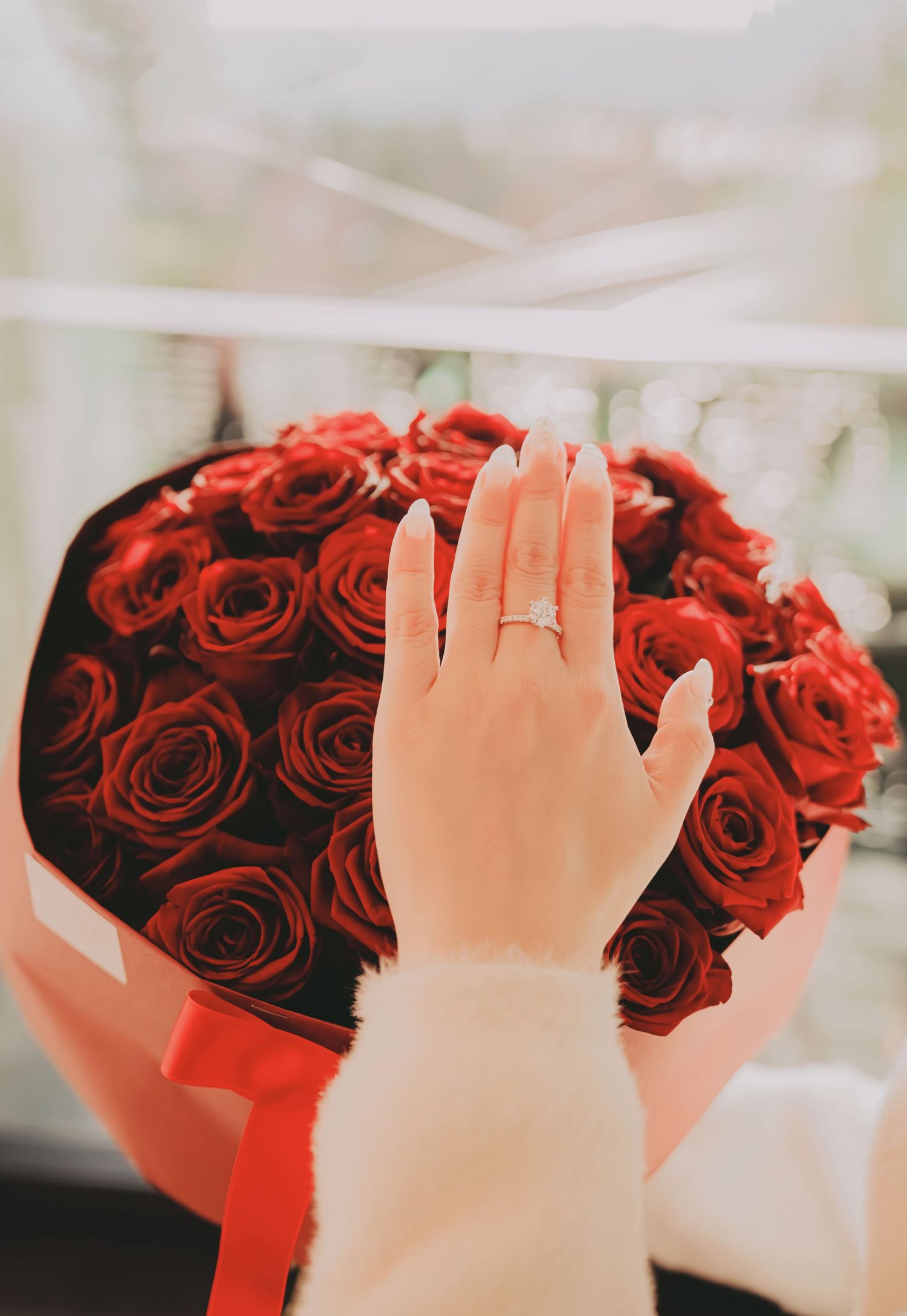 Close-up of a woman's hand with an engagement ring resting on a bouquet of red roses.