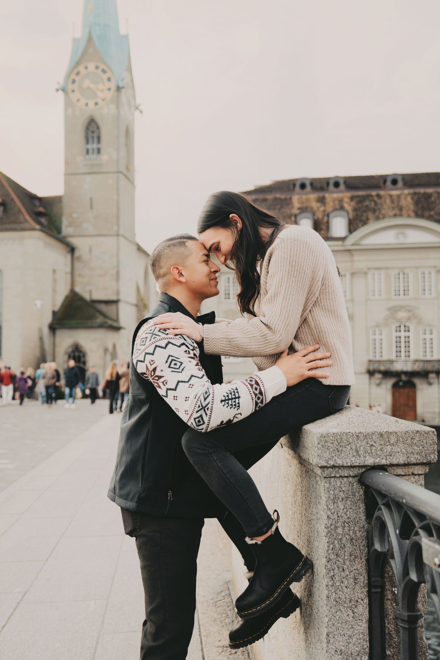 Romantic couple sharing an intimate moment on a stone bridge with a historic church tower in Zurich, Switzerland.