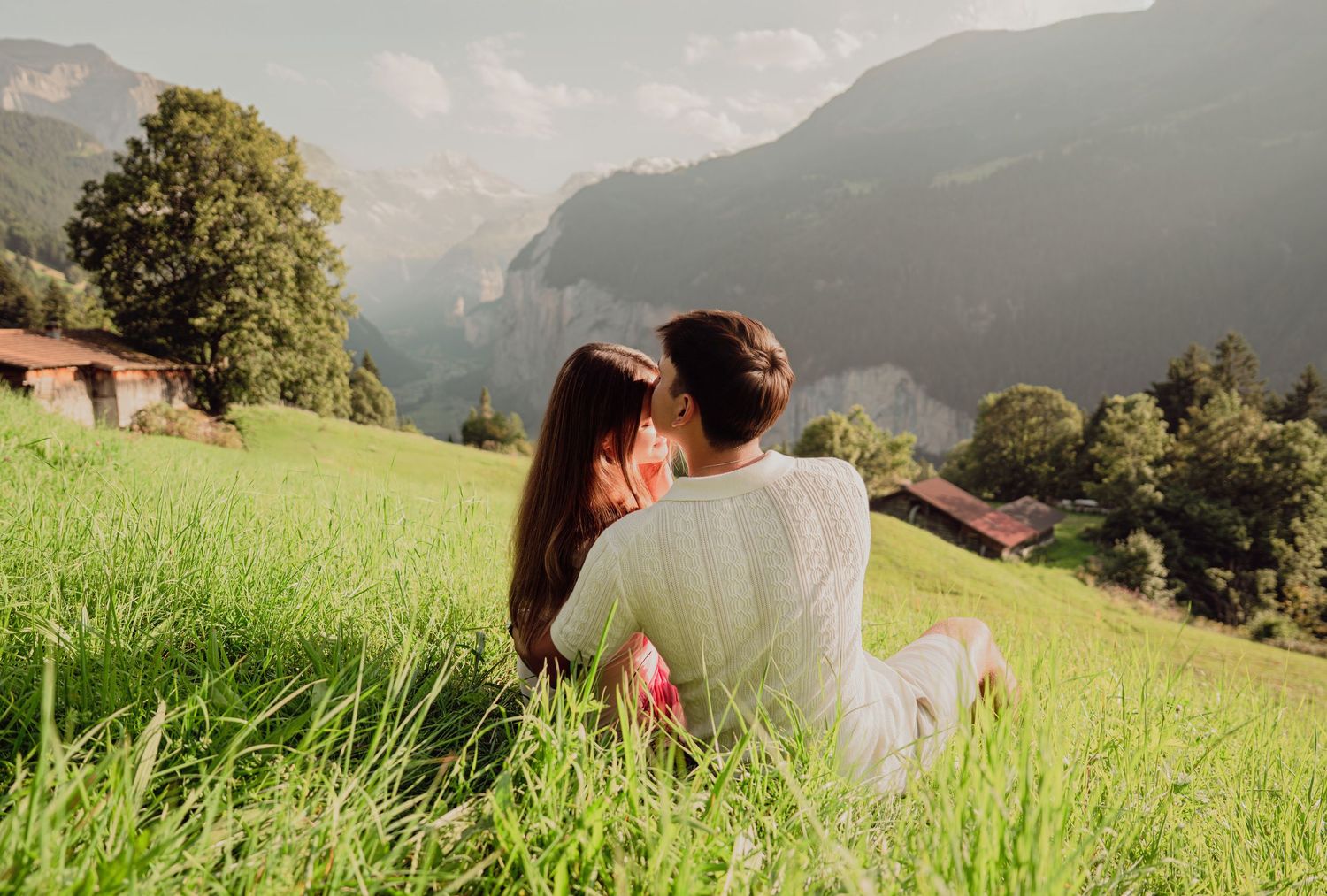 Couple cuddling on lush green hillside overlooking scenic Lauterbrunnen valley in Swiss Alps.