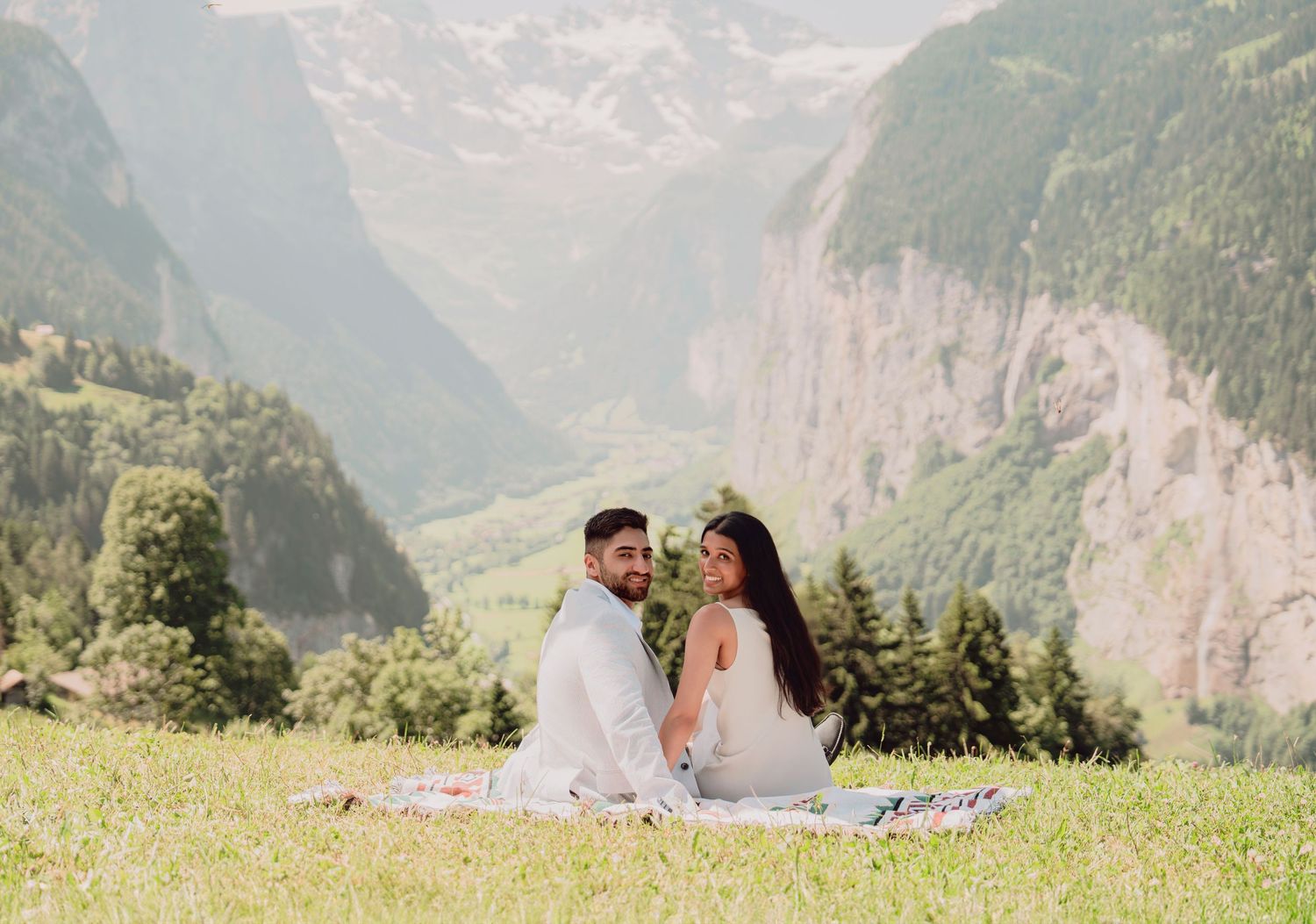 Romantic couple sitting together on a blanket with a breathtaking misty Swiss alpine valley behind them.