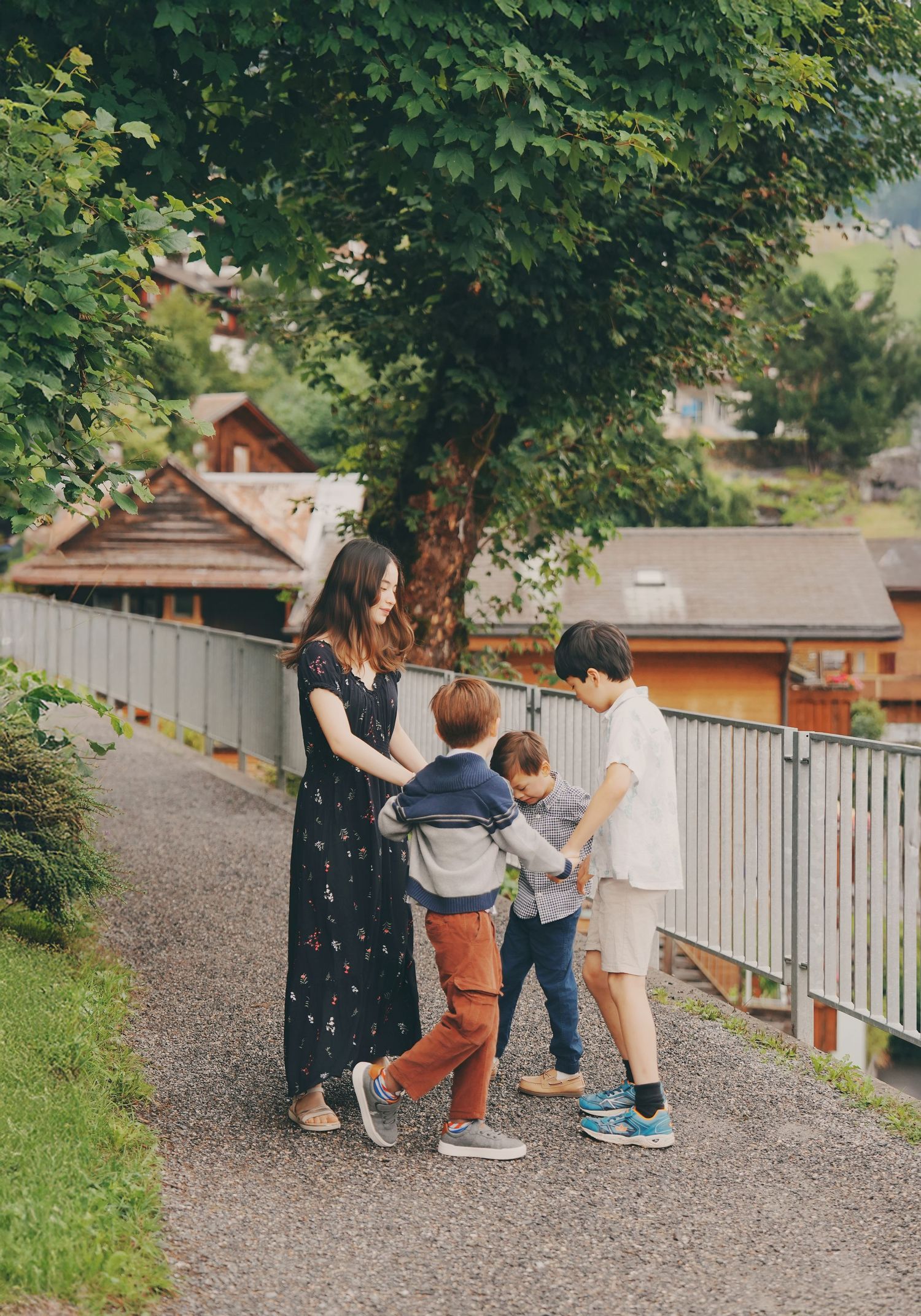 Mother in black floral dress with two young boys playing together on a charming Swiss village path.