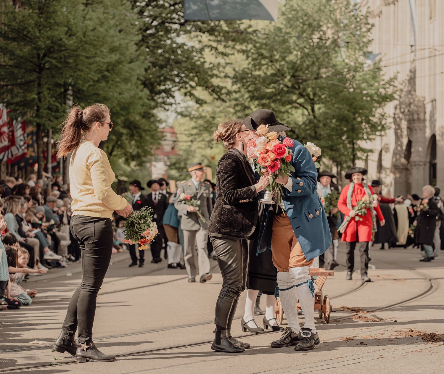 A costumed parade participant bows while offering a bouquet of roses to a woman on a city street.
