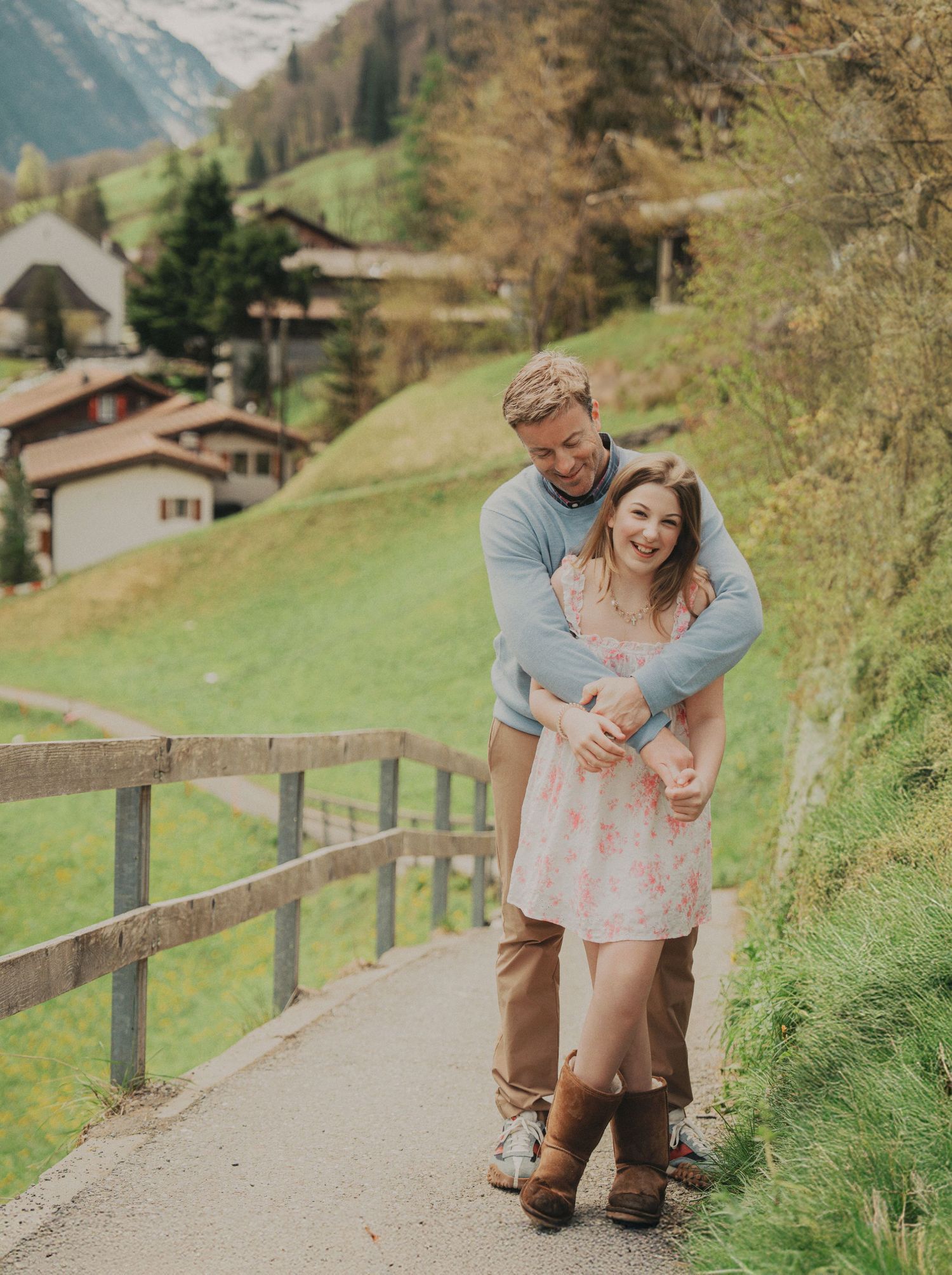 A joyful couple laughs together on a scenic alpine pathway surrounded by lush green Swiss countryside.