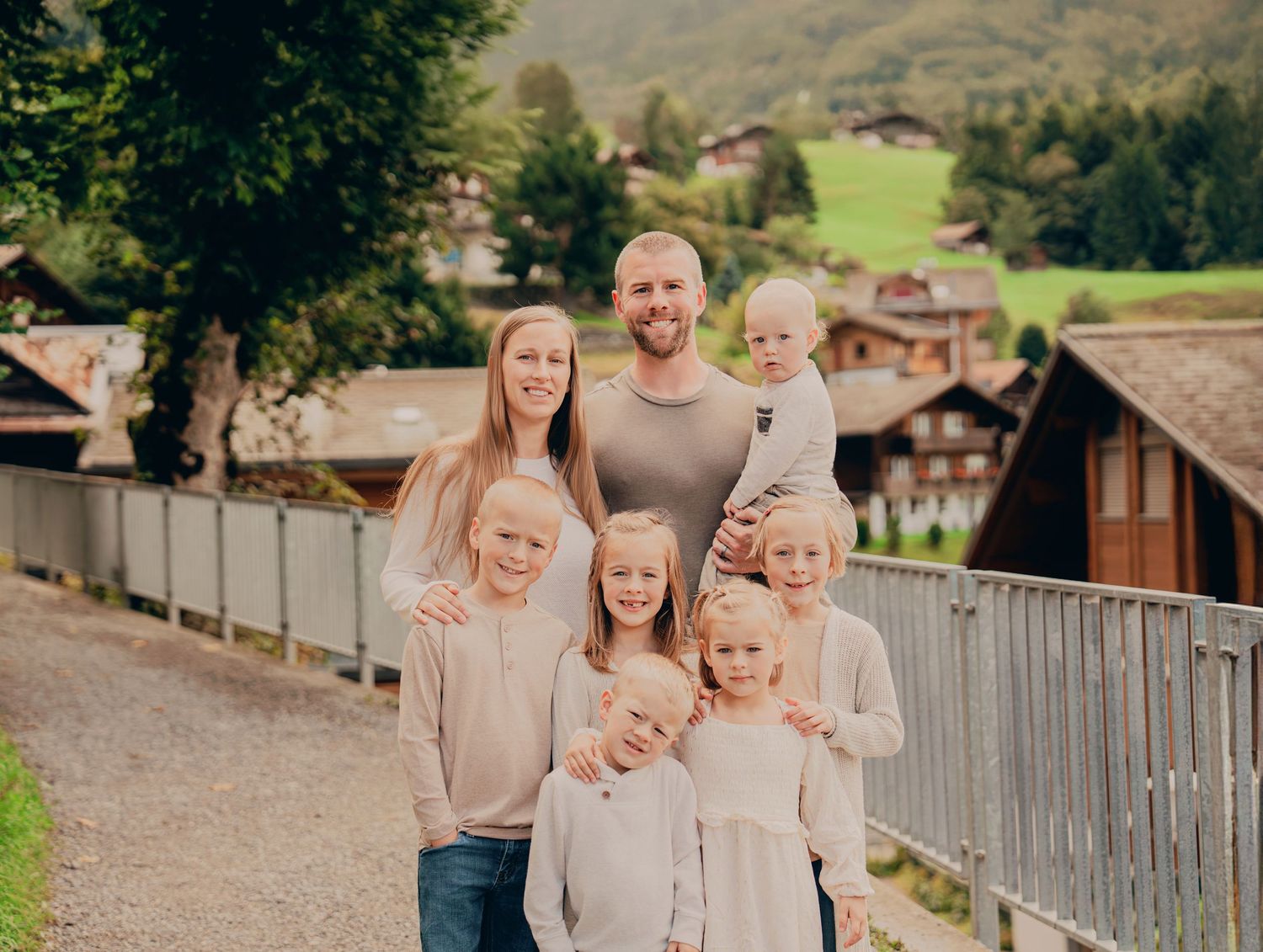 Large family of parents with six young children posing on a path in a scenic Swiss mountain village.