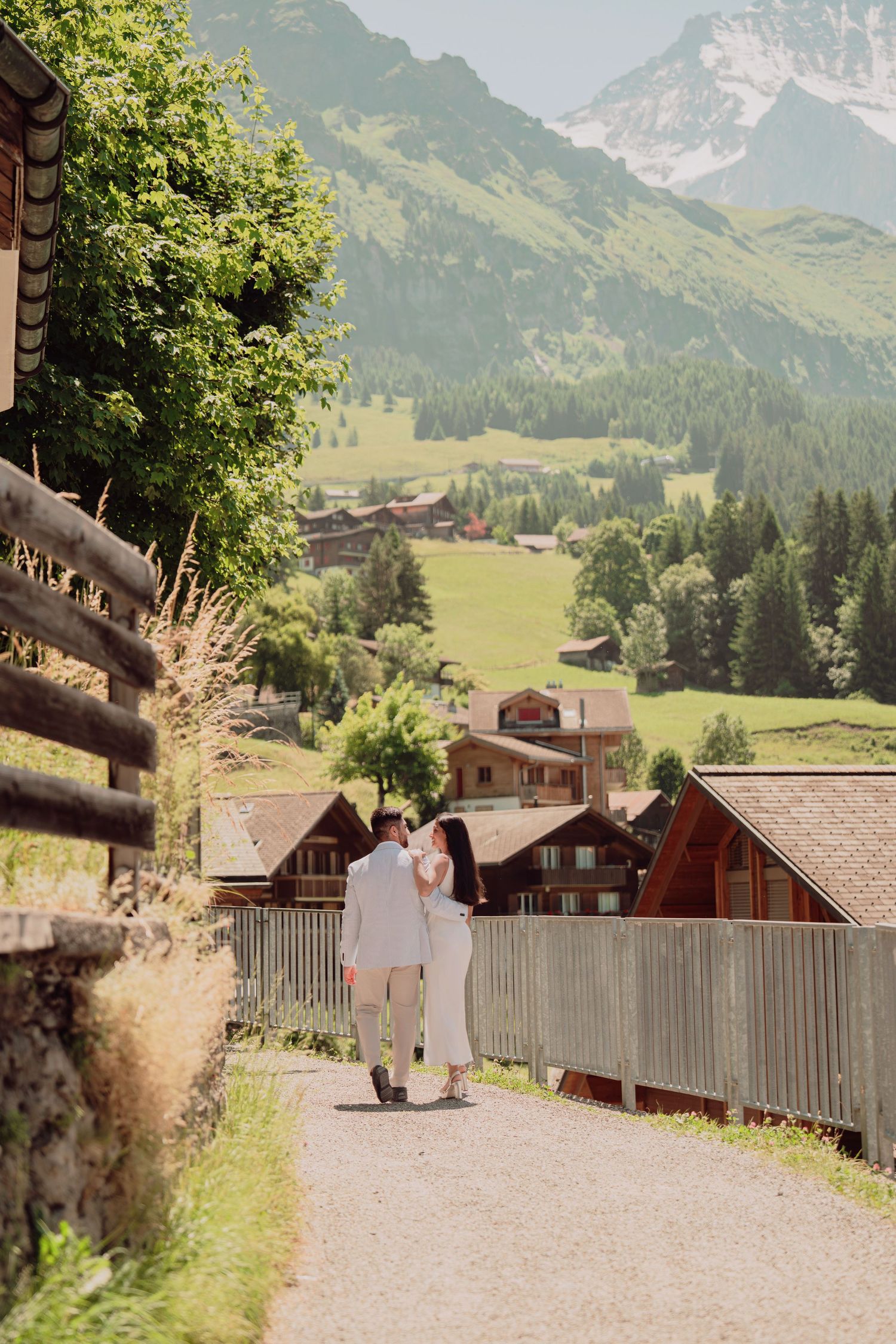 Couple in white wedding attire walking hand in hand through a picturesque Swiss Alpine village.