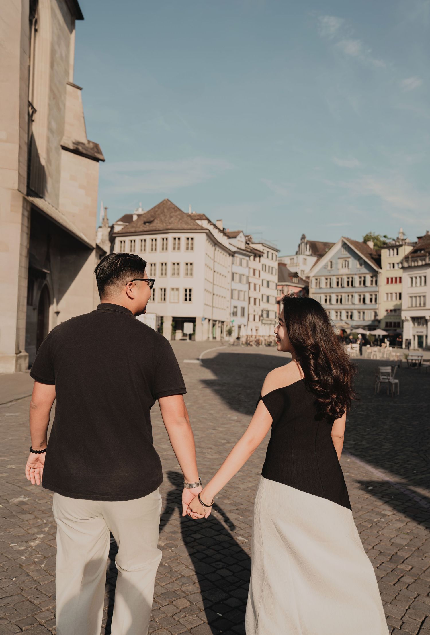 Couple strolling hand in hand through historic cobblestone plaza in Zurich old town.