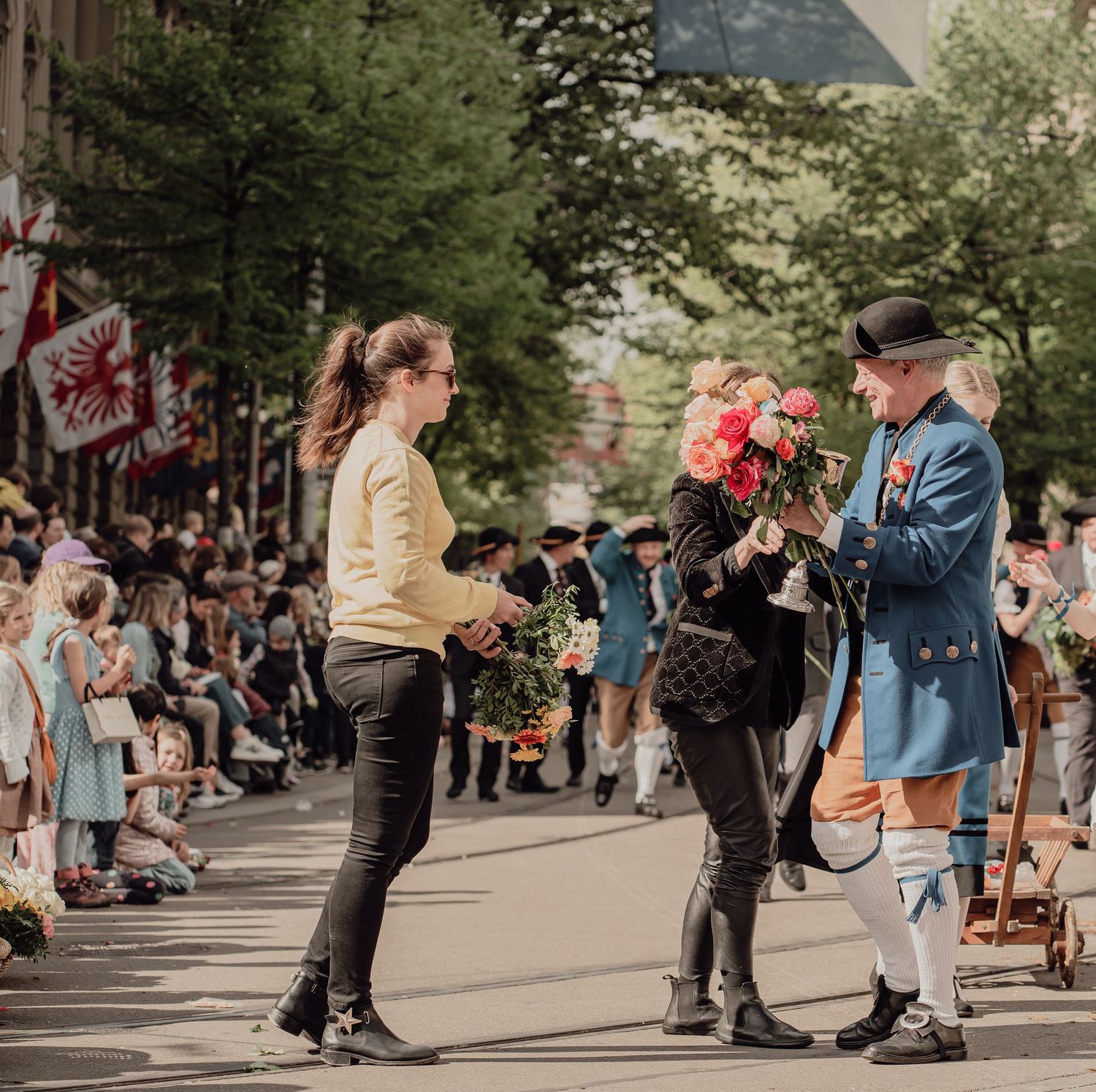 Man in historical blue costume offers flowers to spectators during a traditional outdoor festival.