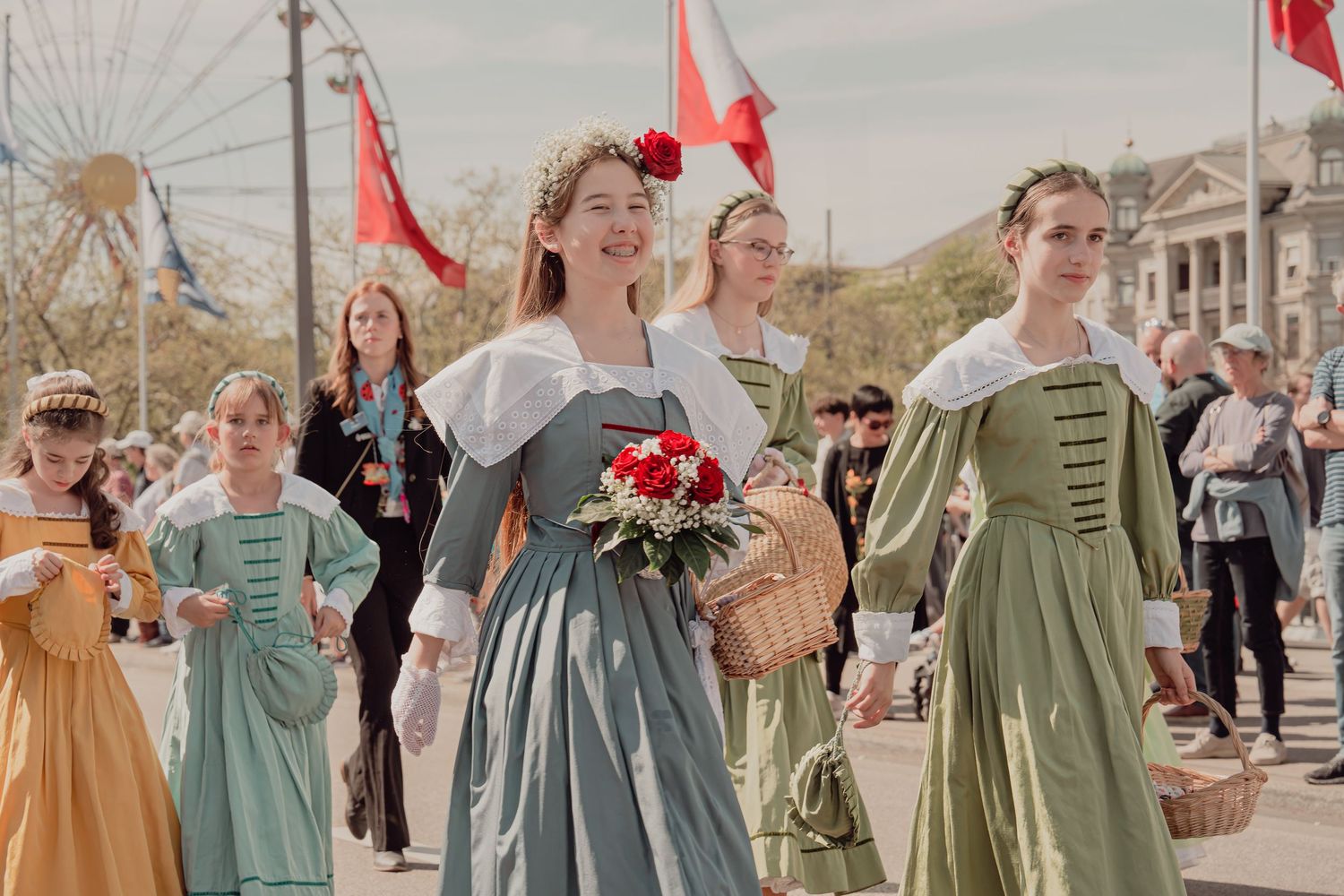 Women and girls in historical Swiss costumes carry flower bouquets during a festive cultural parade.