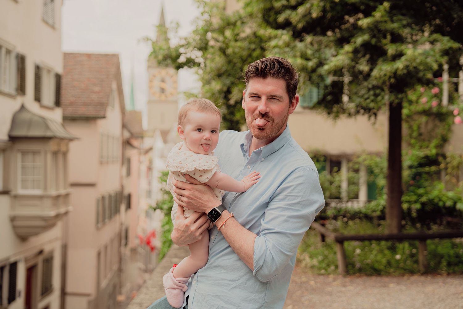 Father making funny face while holding baby in a picturesque European old town street setting.
