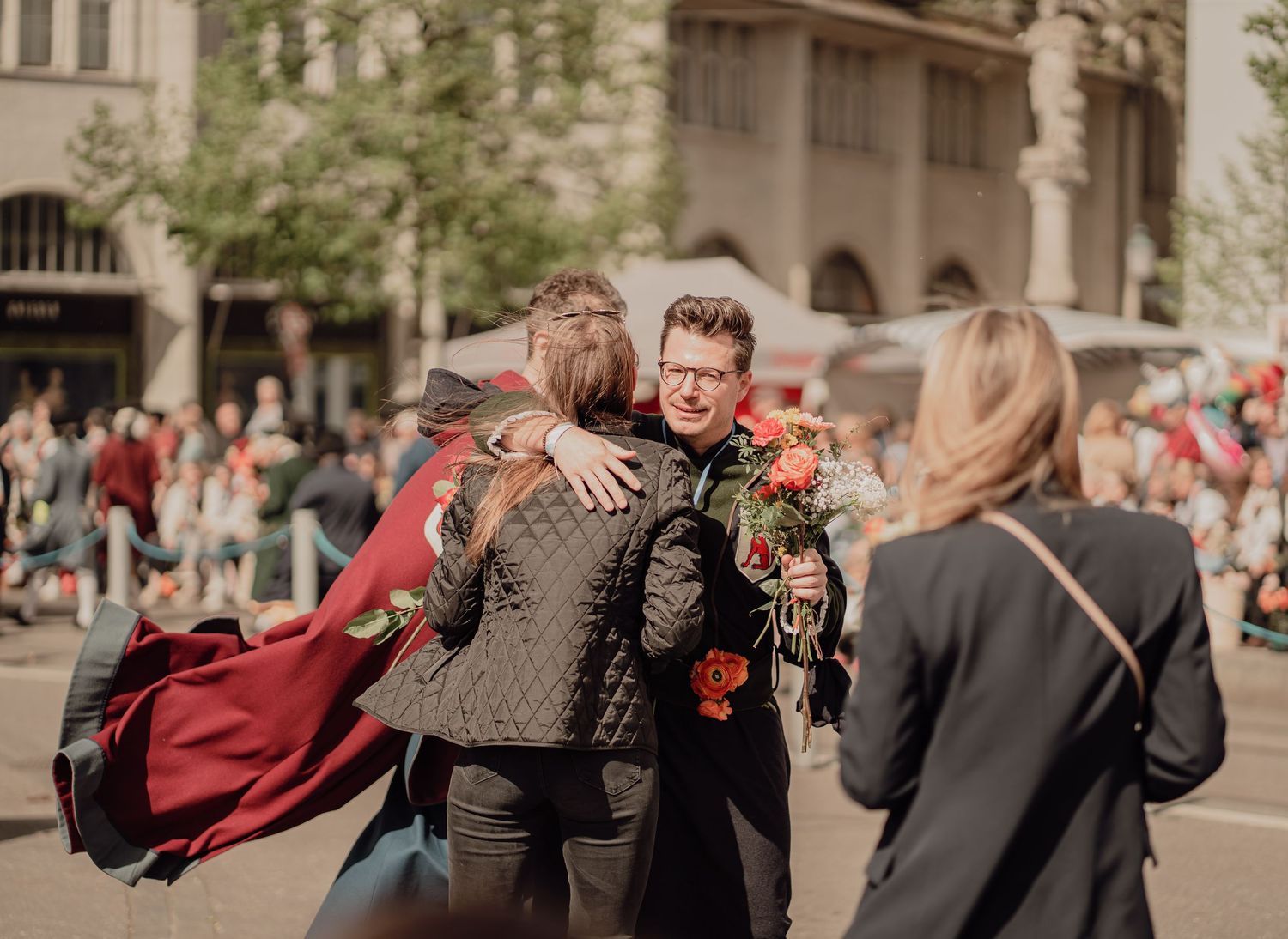 Man holding red roses embracing someone at an outdoor street celebration event.