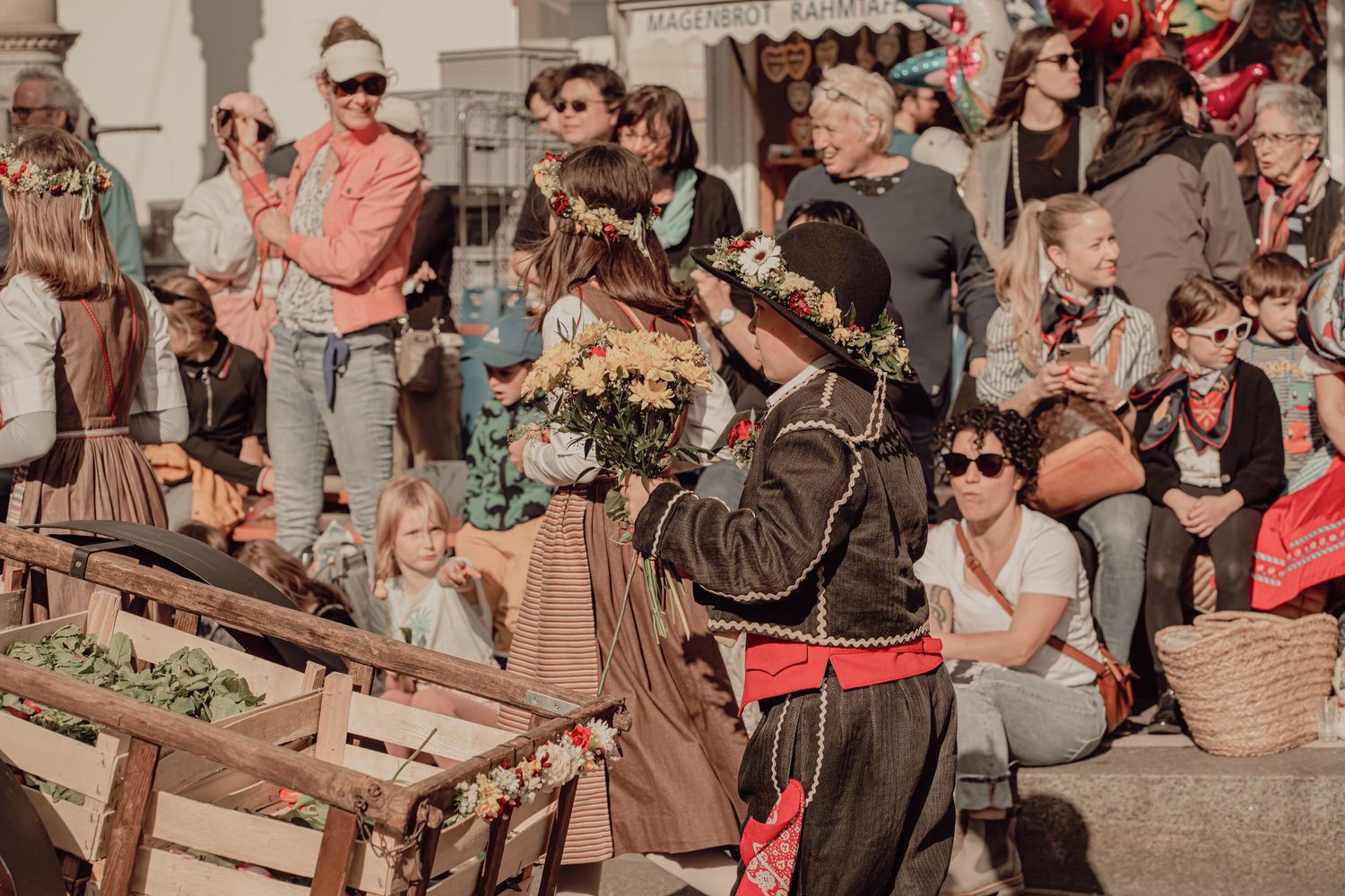 A performer in traditional costume holds flowers while entertaining a crowd at an outdoor cultural festival.