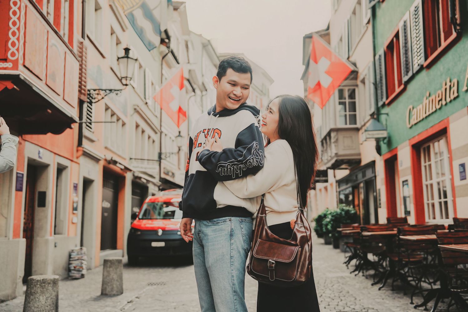 A happy couple embraces on a charming cobblestone street in Zurich's old town with colorful buildings.