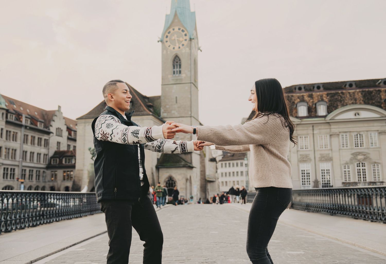 Couple dancing on a bridge in Zurich with Fraumunster church tower in background.