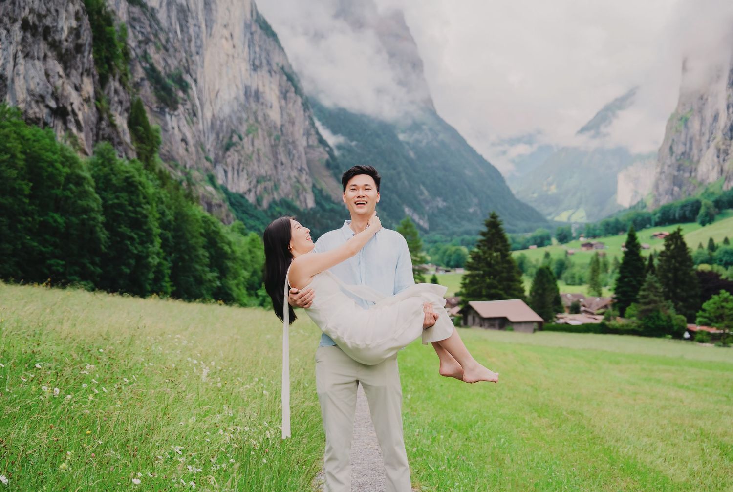 Man lifts woman joyfully in blooming alpine meadow with stunning Lauterbrunnen valley mountain backdrop.
