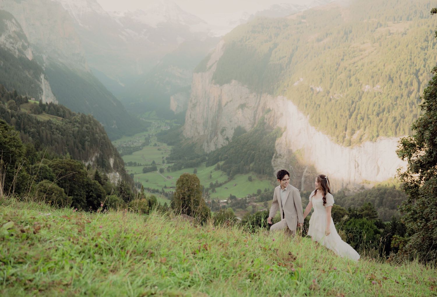 Bride and groom holding hands on a lush hillside overlooking the breathtaking Lauterbrunnen valley in Switzerland.