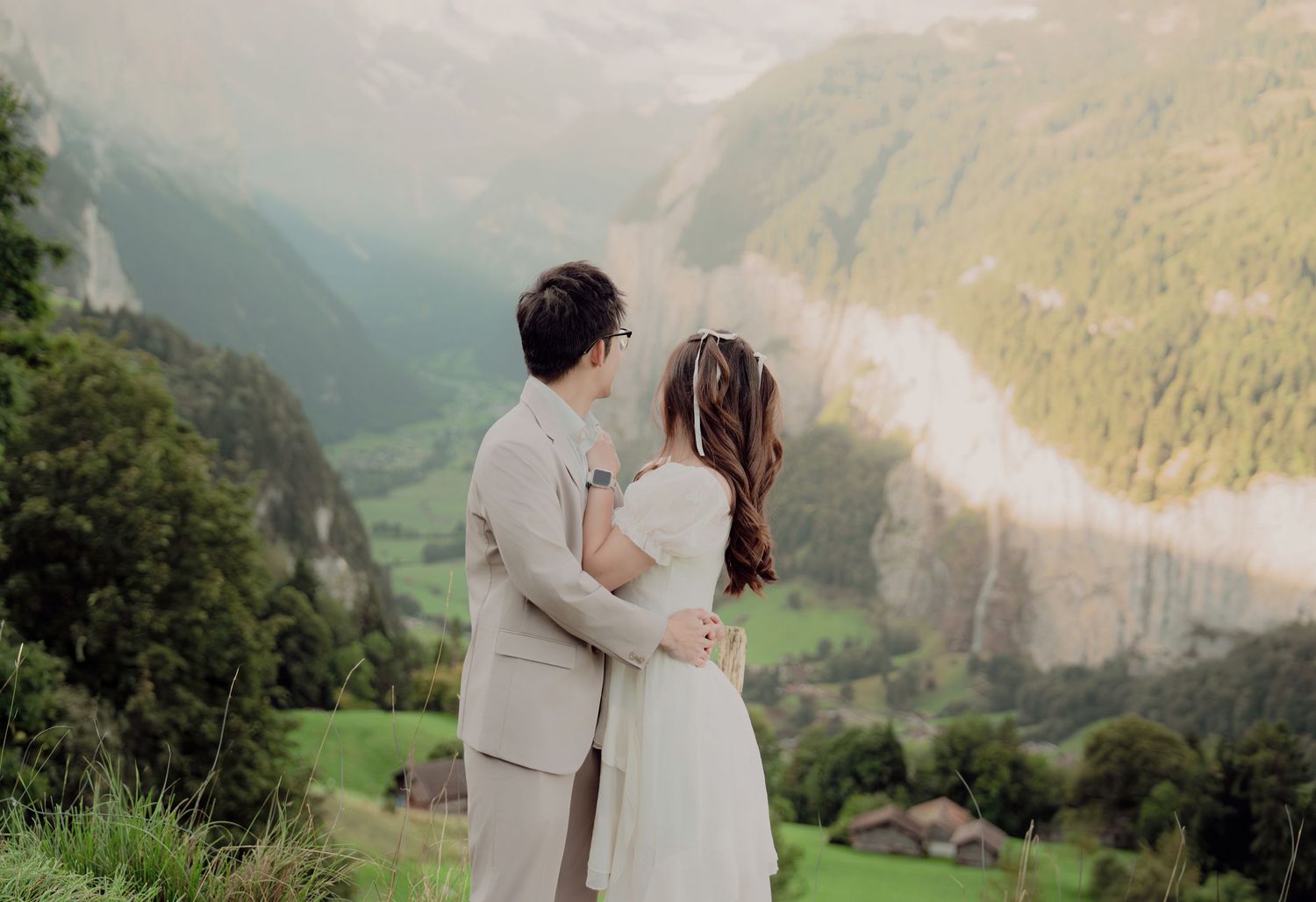Couple embracing on a scenic Swiss hillside with the majestic Lauterbrunnen valley and misty mountains behind them.