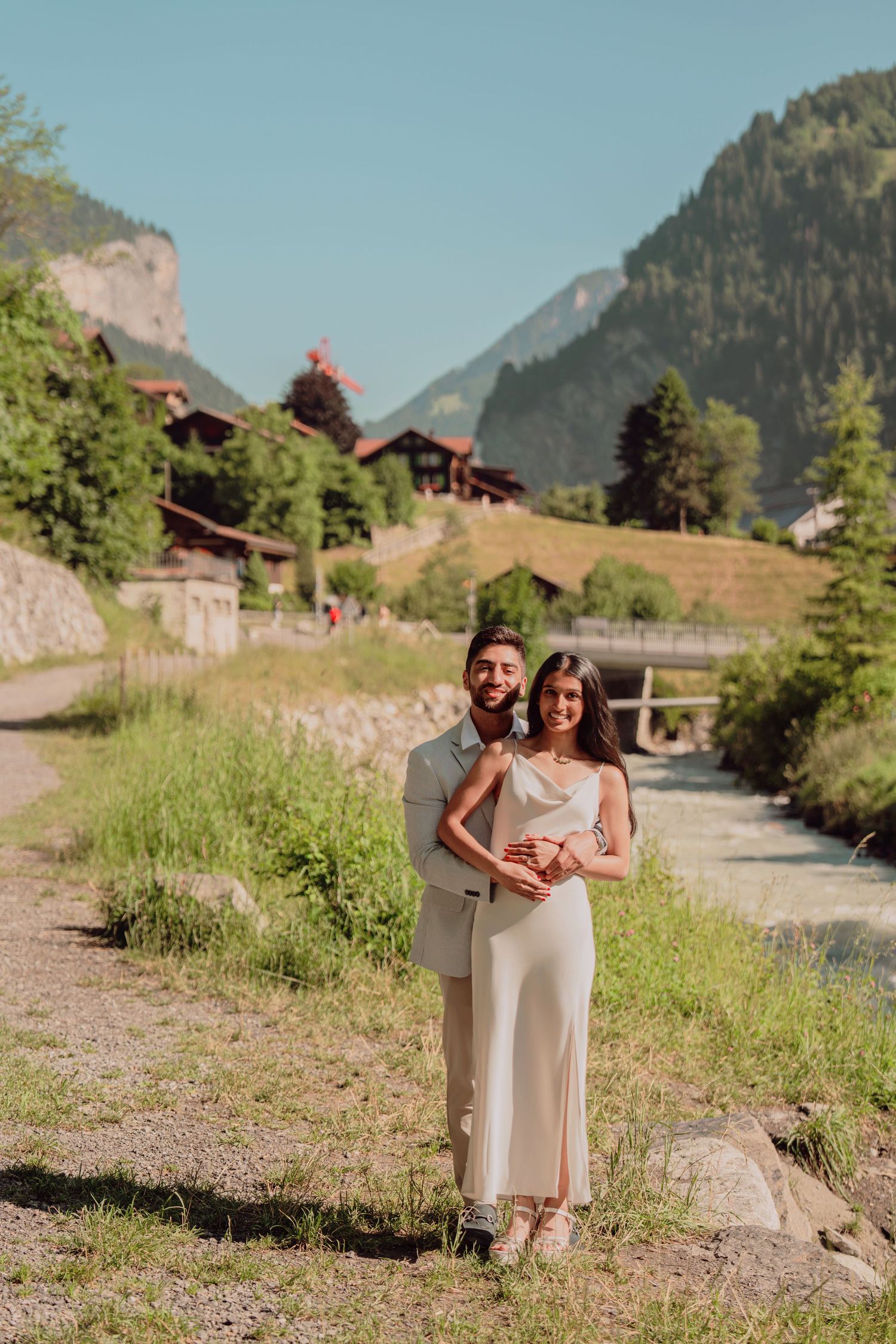 Couple in formal wear holding hands by a mountain stream in a Swiss valley.