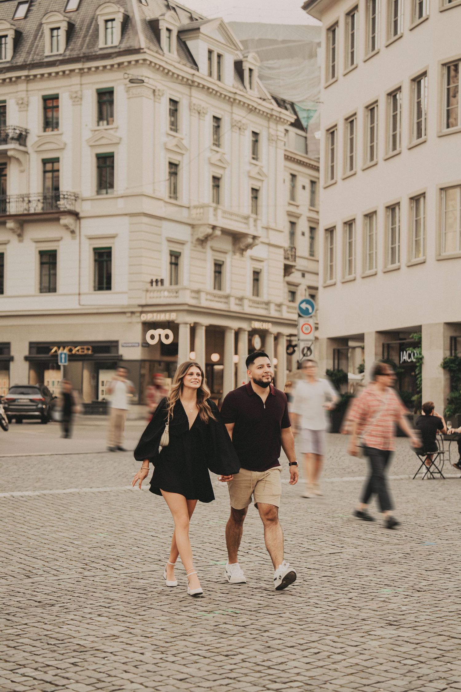 Couple walking hand in hand across cobblestone plaza in Zurich city center.