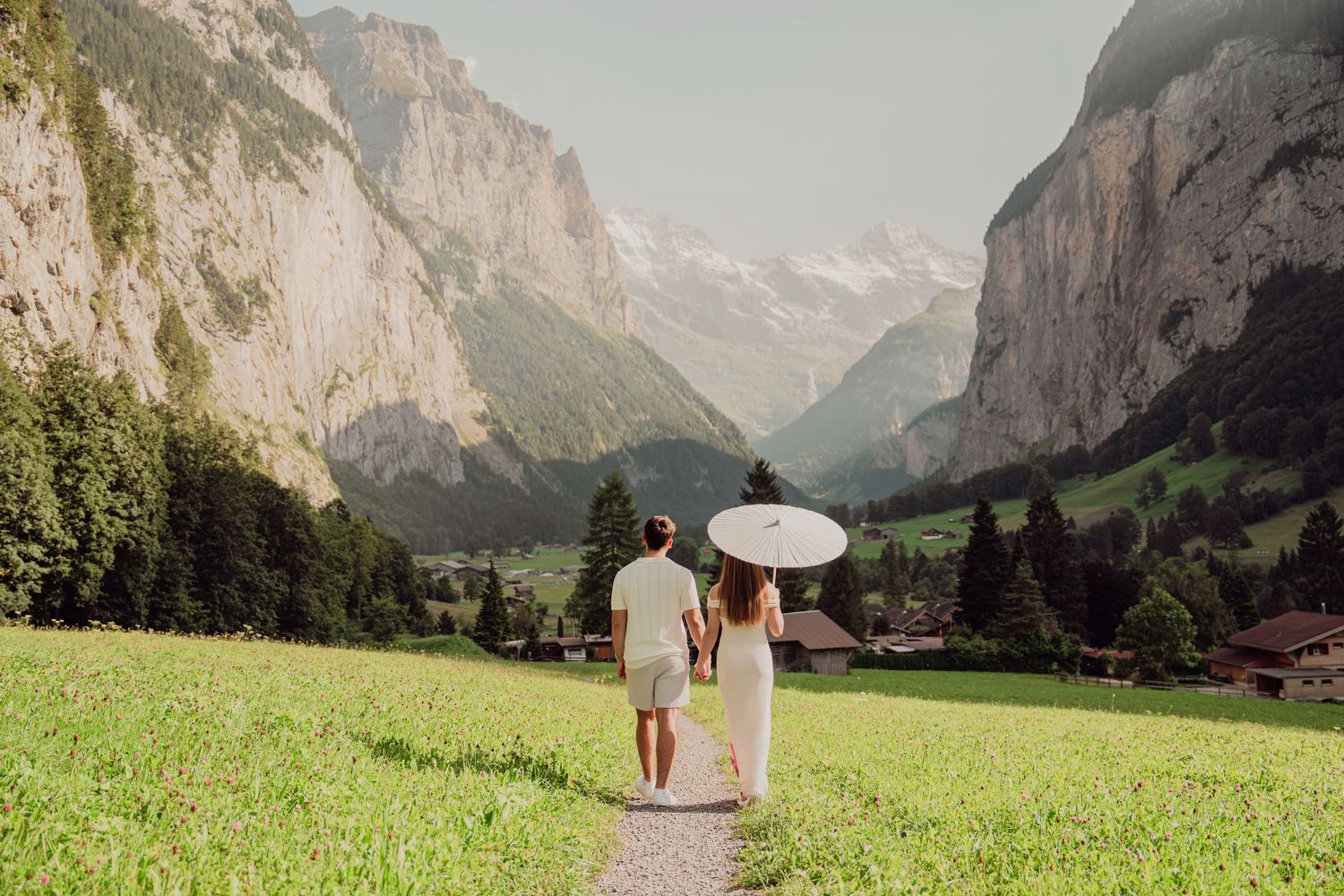 Couple strolling with a white umbrella along a path through a breathtaking Swiss alpine valley.