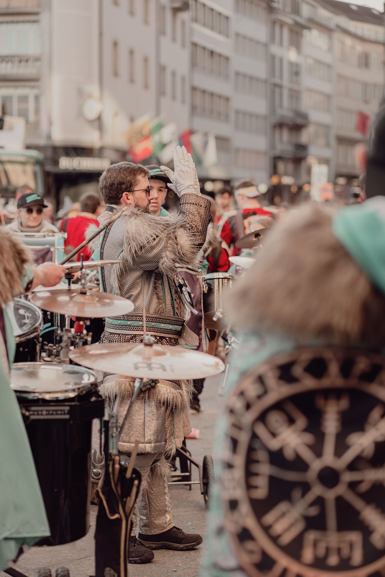 A drummer in a fur costume plays a drum kit on a busy street during a festival.