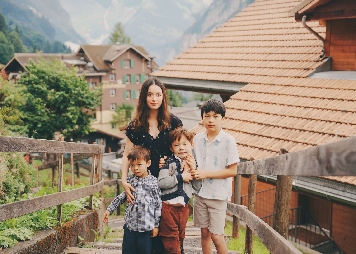 A woman and three boys stand together on a wooden walkway in a charming Swiss mountain village.