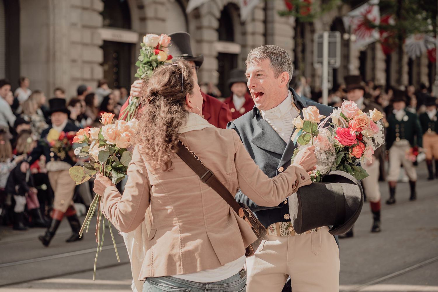 Two people in historical costumes exchanging colorful flower bouquets during an outdoor street festival.